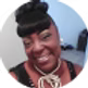 Woman with dark skin smiling, hair in bun, bangs, wearing necklace.