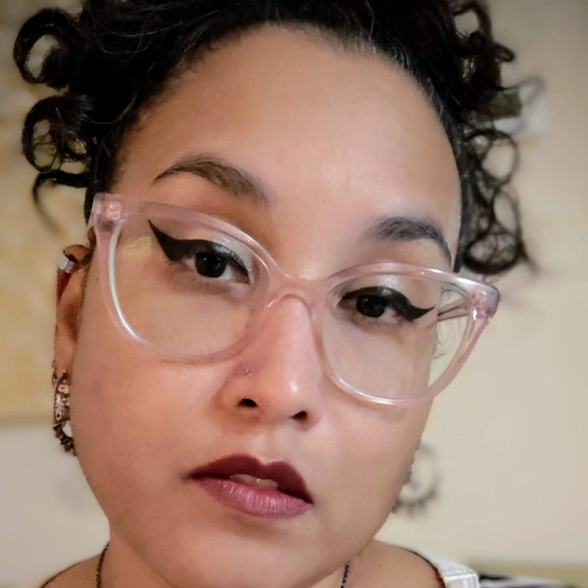 Person wearing pink glasses and a striped shirt, posing indoors with a neutral expression.
