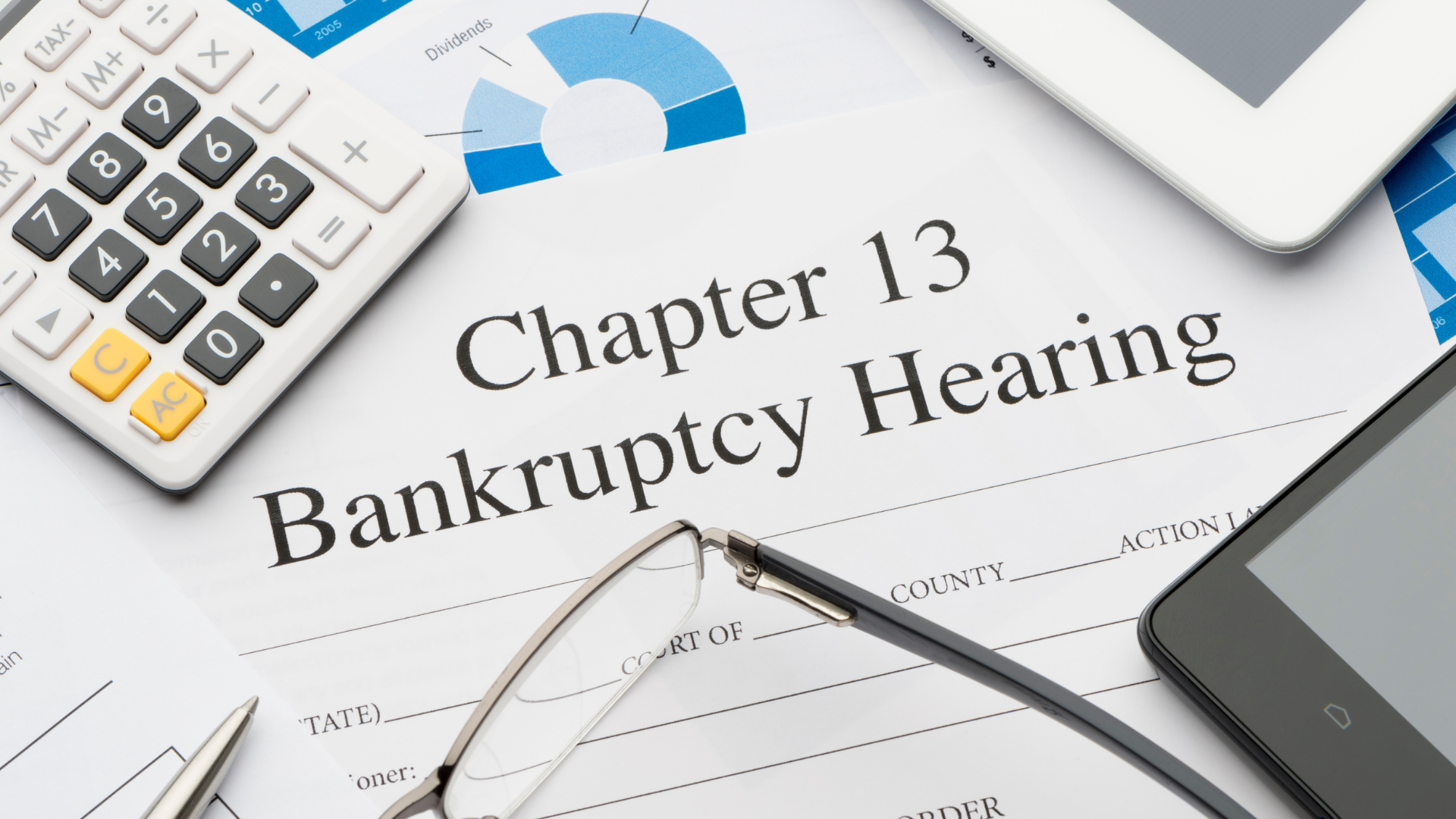 A calculator , glasses , a tablet , and a chapter 13 bankruptcy hearing document are on a table.