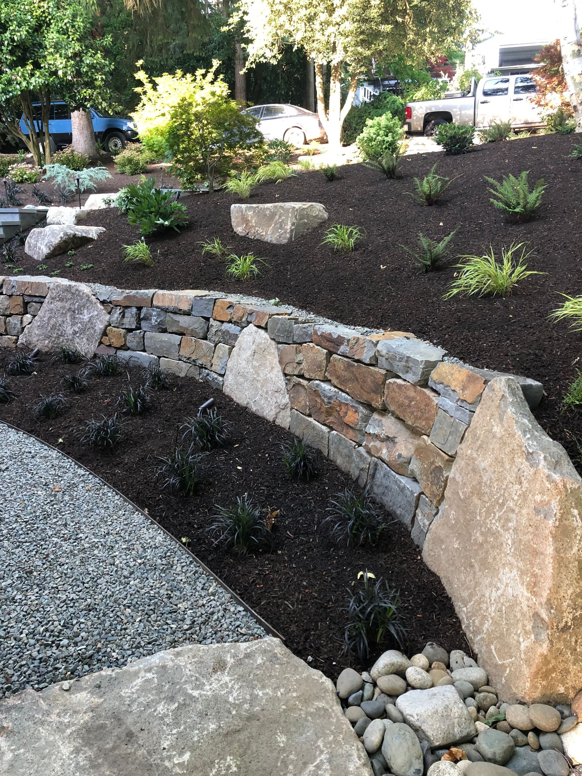Stone retaining wall with plants and gravel landscaping.