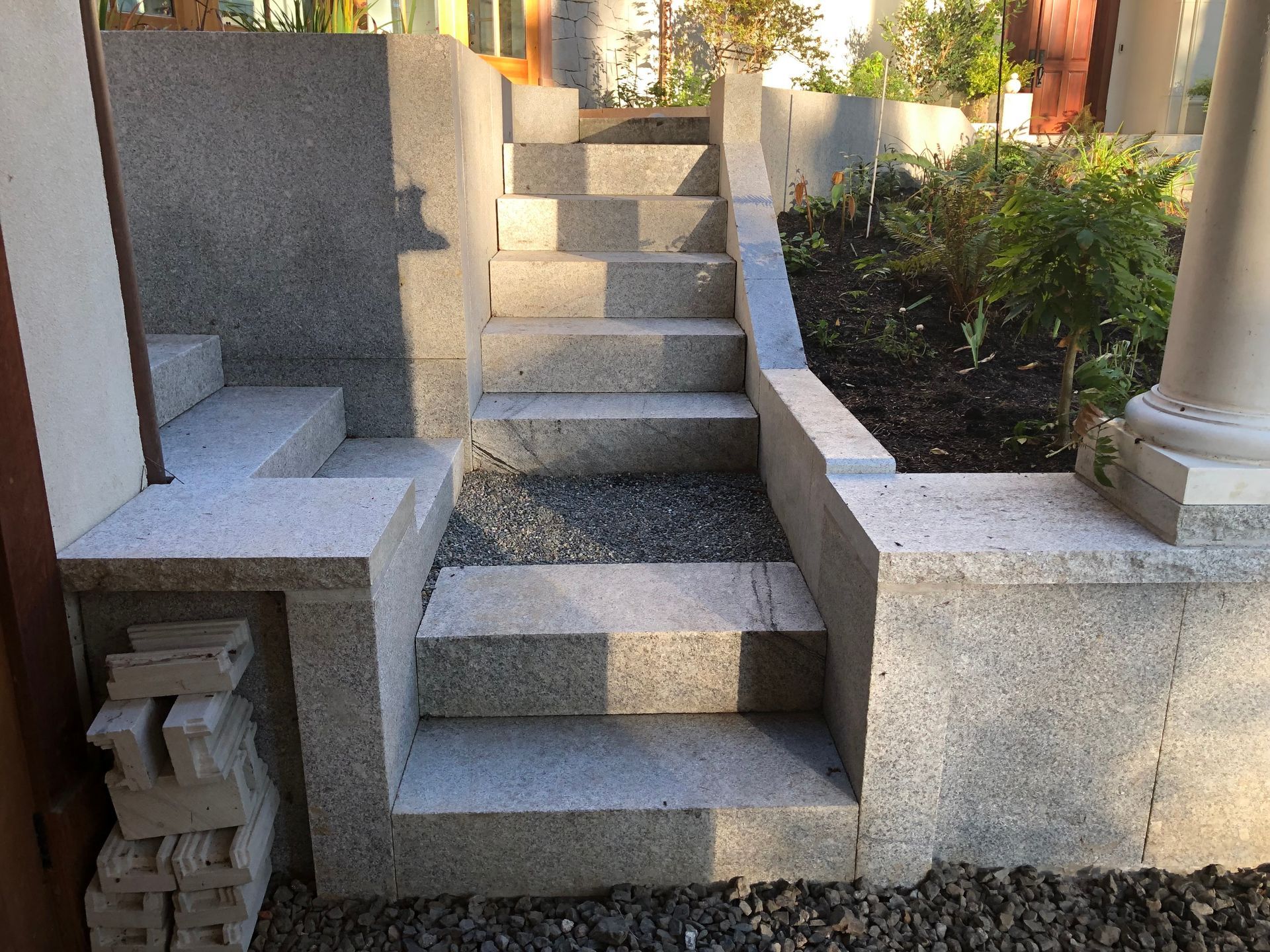 Stone steps leading up, with gray stone retaining walls, a column, and gravel.