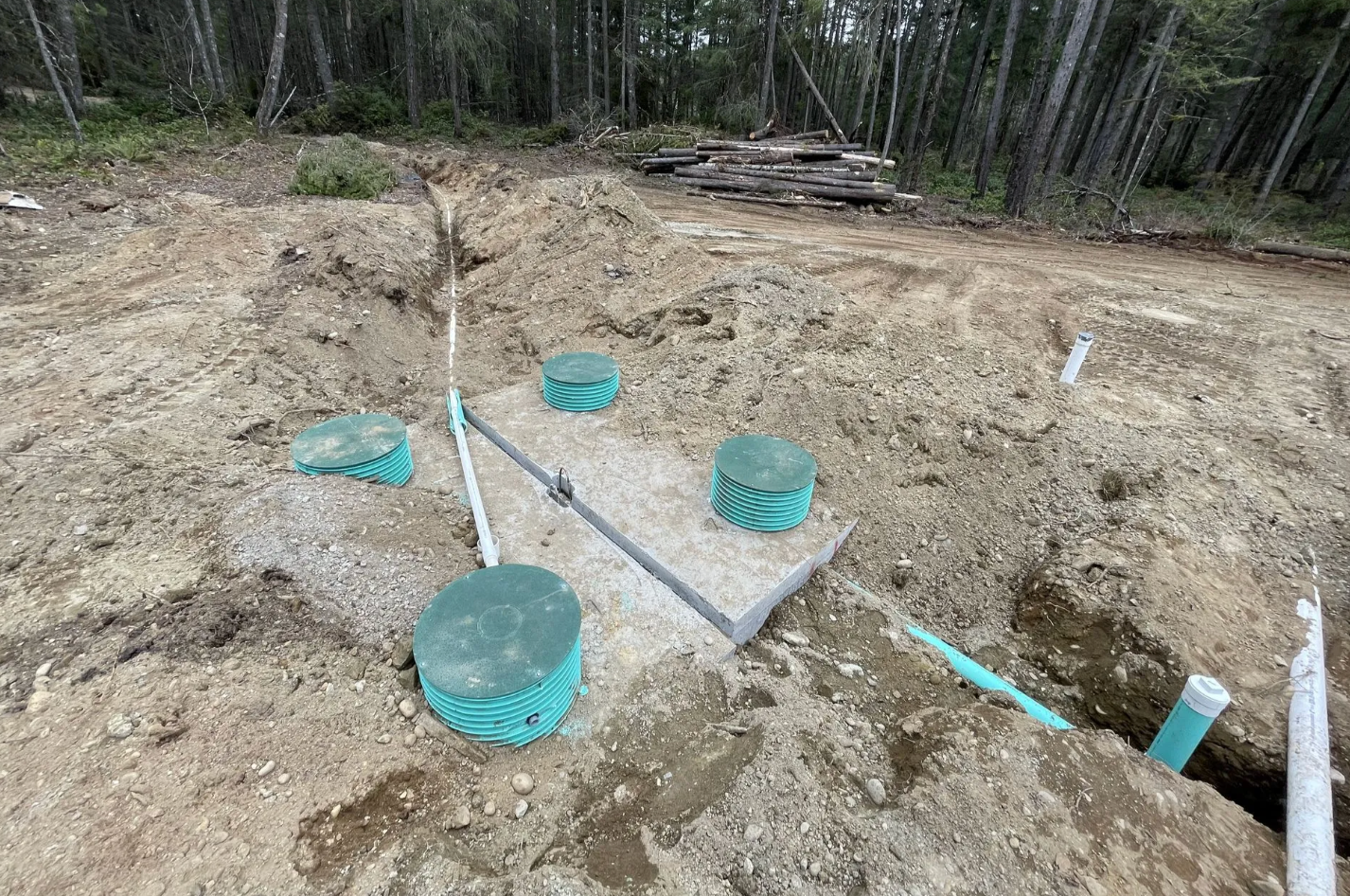 Septic system installation site with exposed gray concrete, green lids, and pipes in dirt.