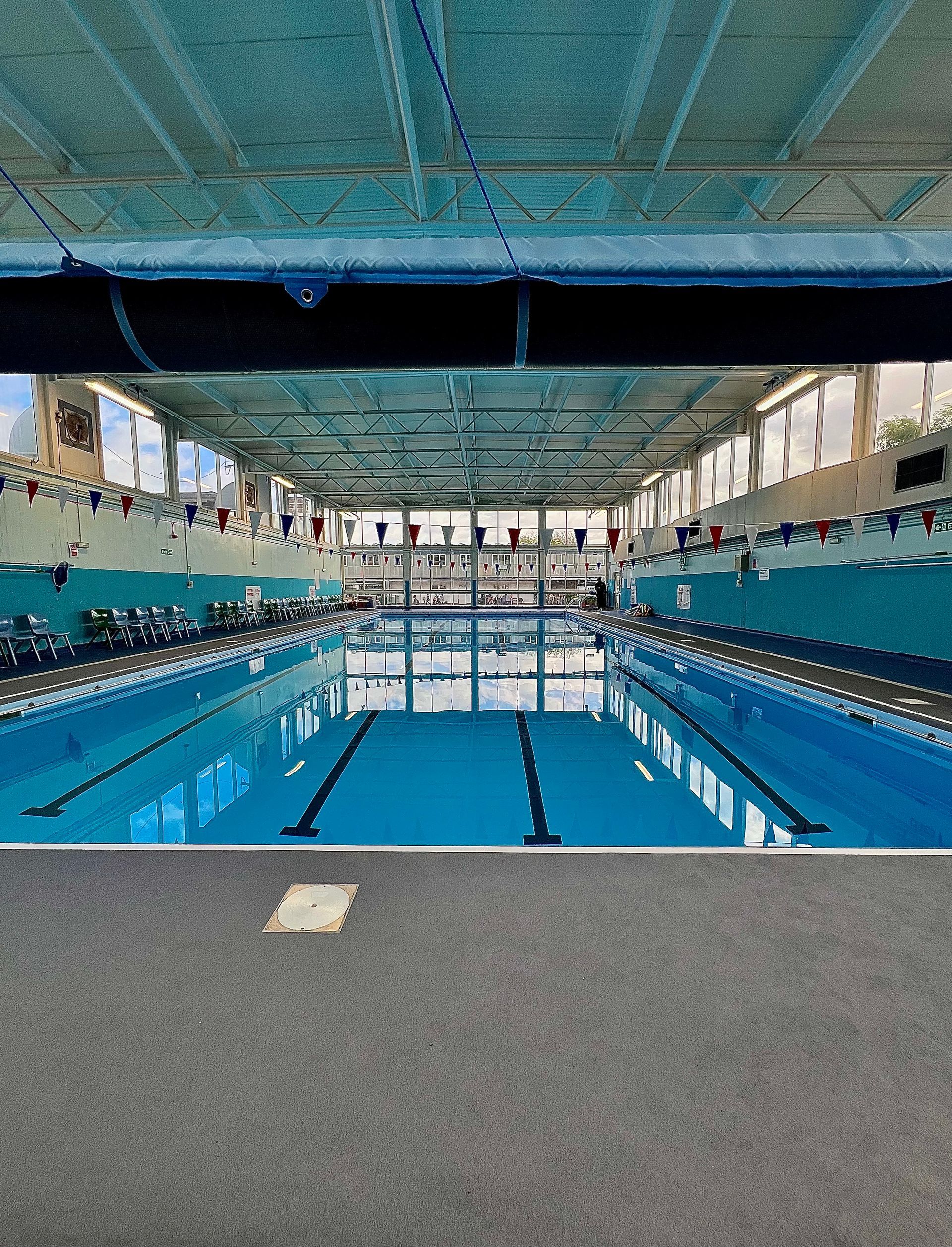 Indoor swimming pool with blue lanes and a high ceiling, viewed from the end of the deck.