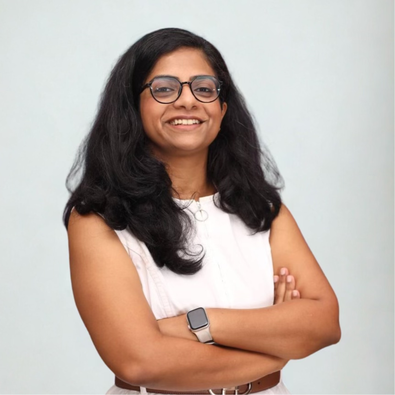 Smiling person with glasses and crossed arms, wearing a white sleeveless top against a light background