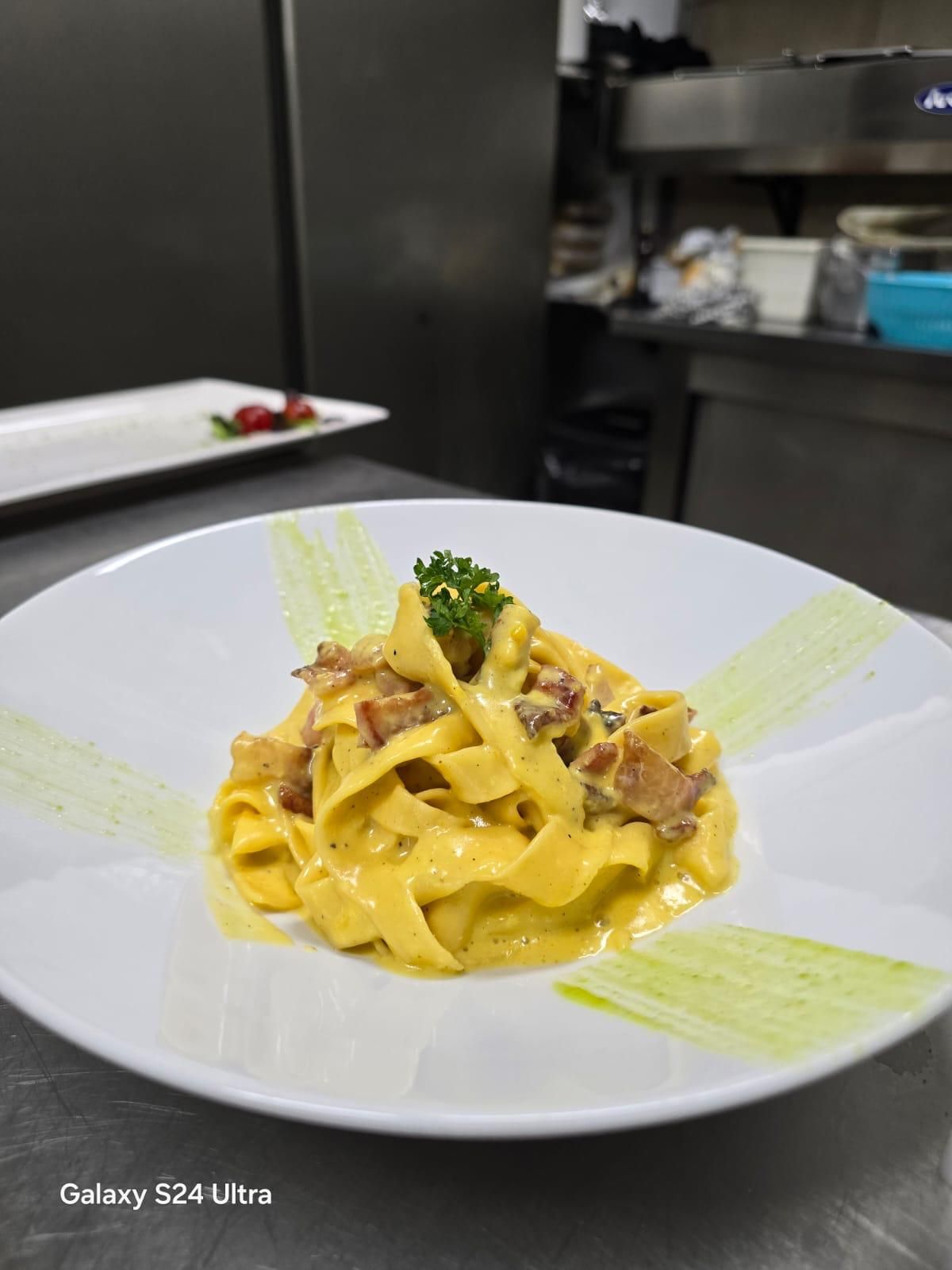 Pasta alla carbonara in una ciotola bianca, guarnita con prezzemolo. Ambiente cucina.