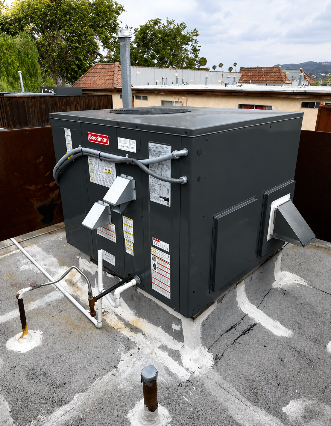 Black rooftop HVAC unit with vents, pipes, and labels on a gravel-covered roof.