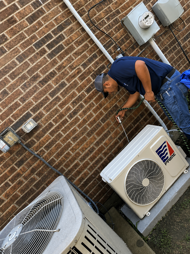 Technician servicing an outdoor HVAC unit beside a brick wall with utility boxes.