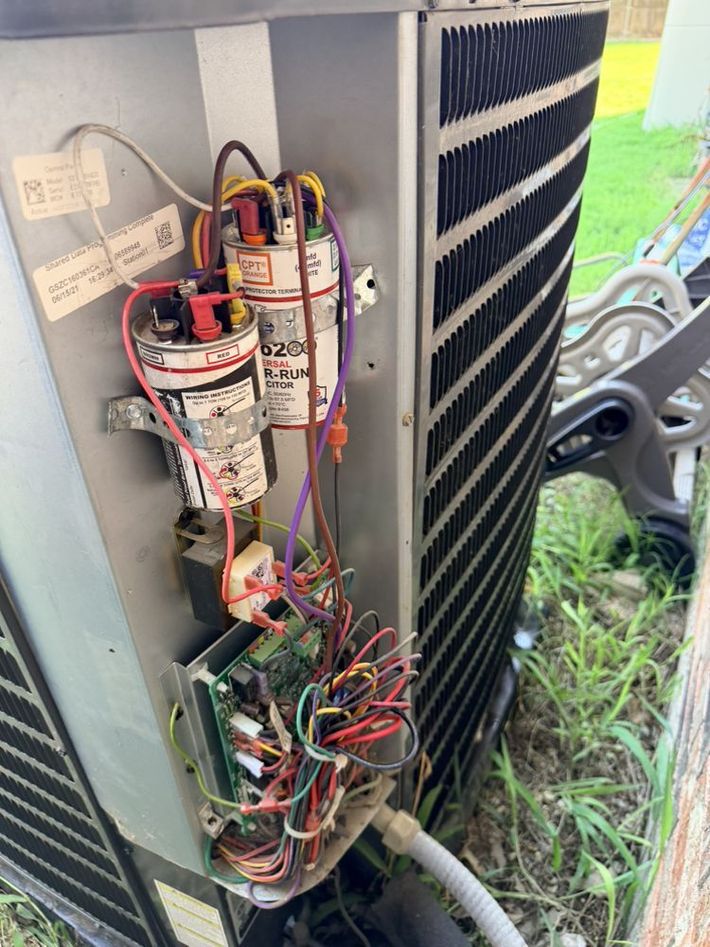 Open electrical panel with exposed wires and components on the side of an HVAC unit.