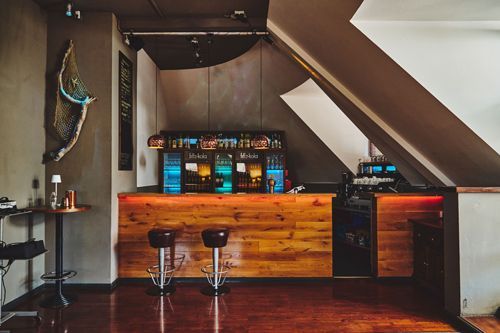 Hölzerne Bar unter einer Dachscräge. Davor zwei Barhocker