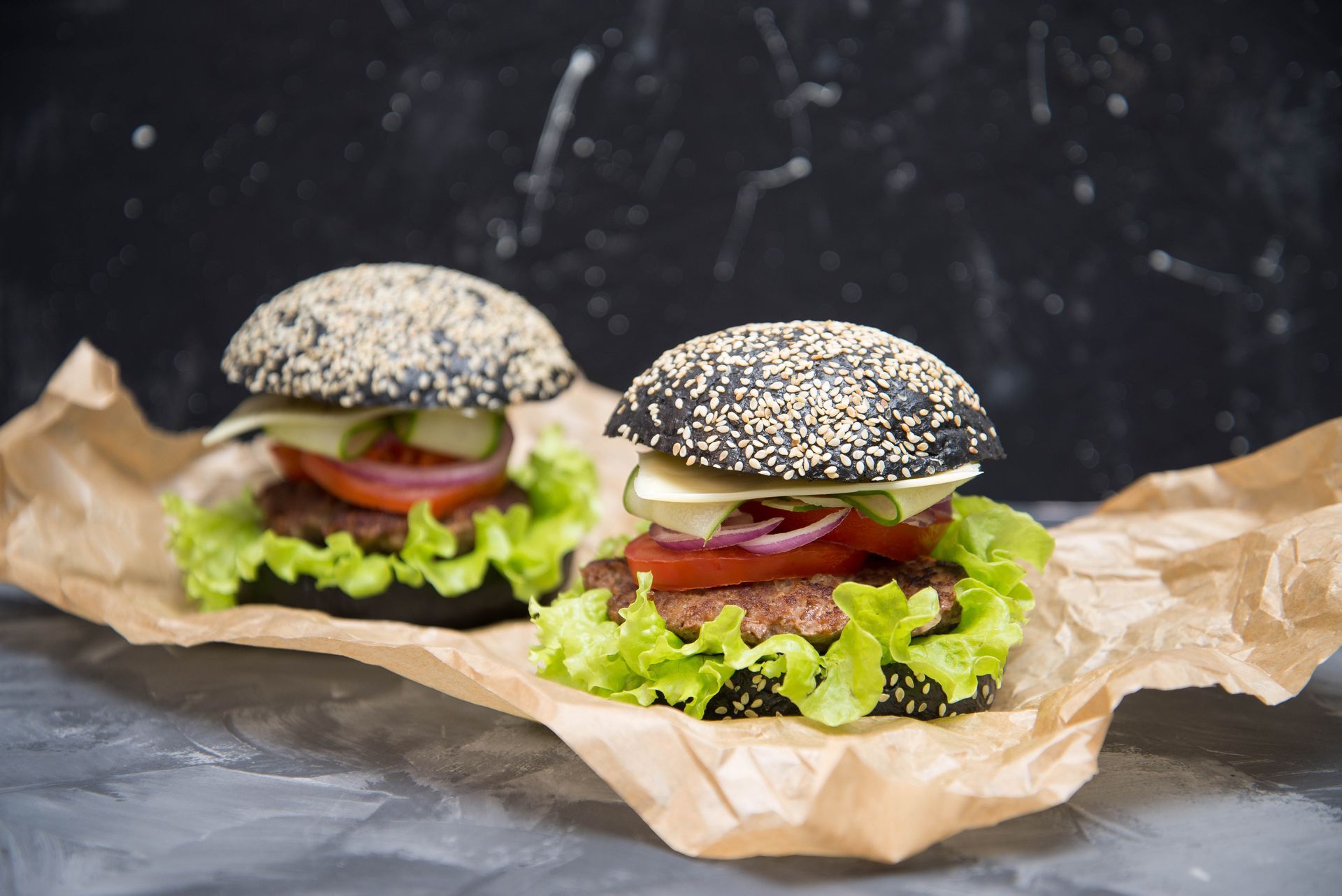 Burger in einem schwarzen Sesam-Burgerbrötchen mit Salat und Gurke. Auf einem Papier liegend