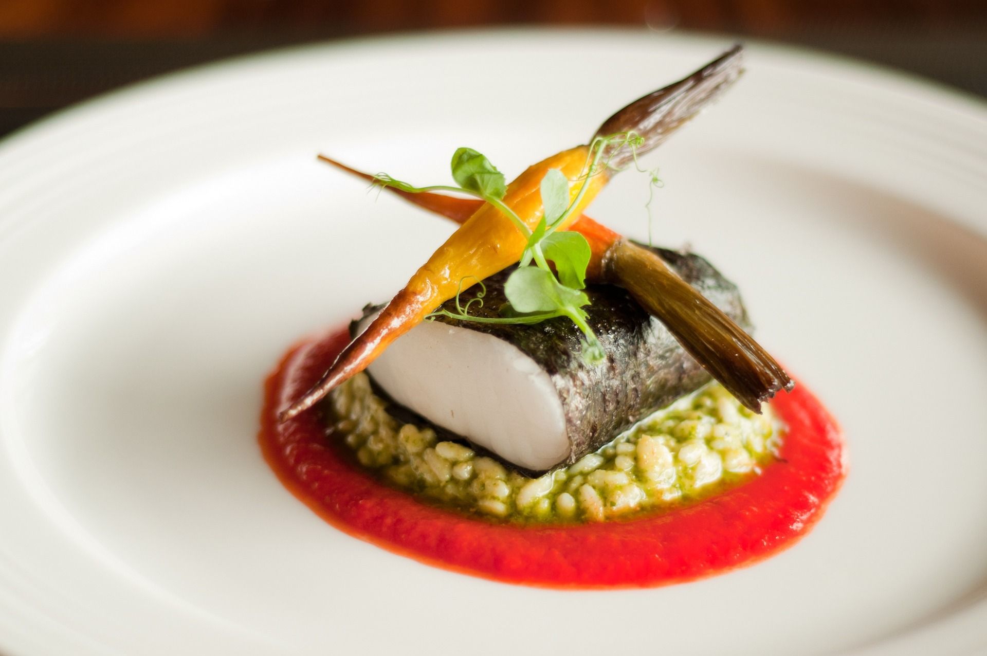 Fine-Dining Teller: Graupenrisotto auf einem Spiegel mit roter Soße, Fisch im Algenblatt, darauf Babymöhren