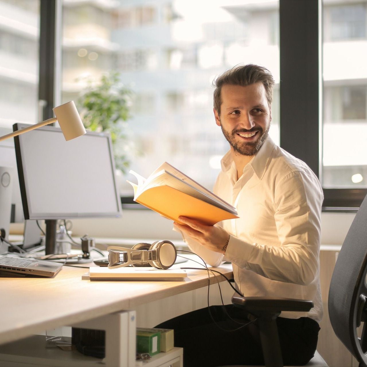 Blonder Mann sitzt am Schreibtisch, vor einem PC und lächelt in die Kamera