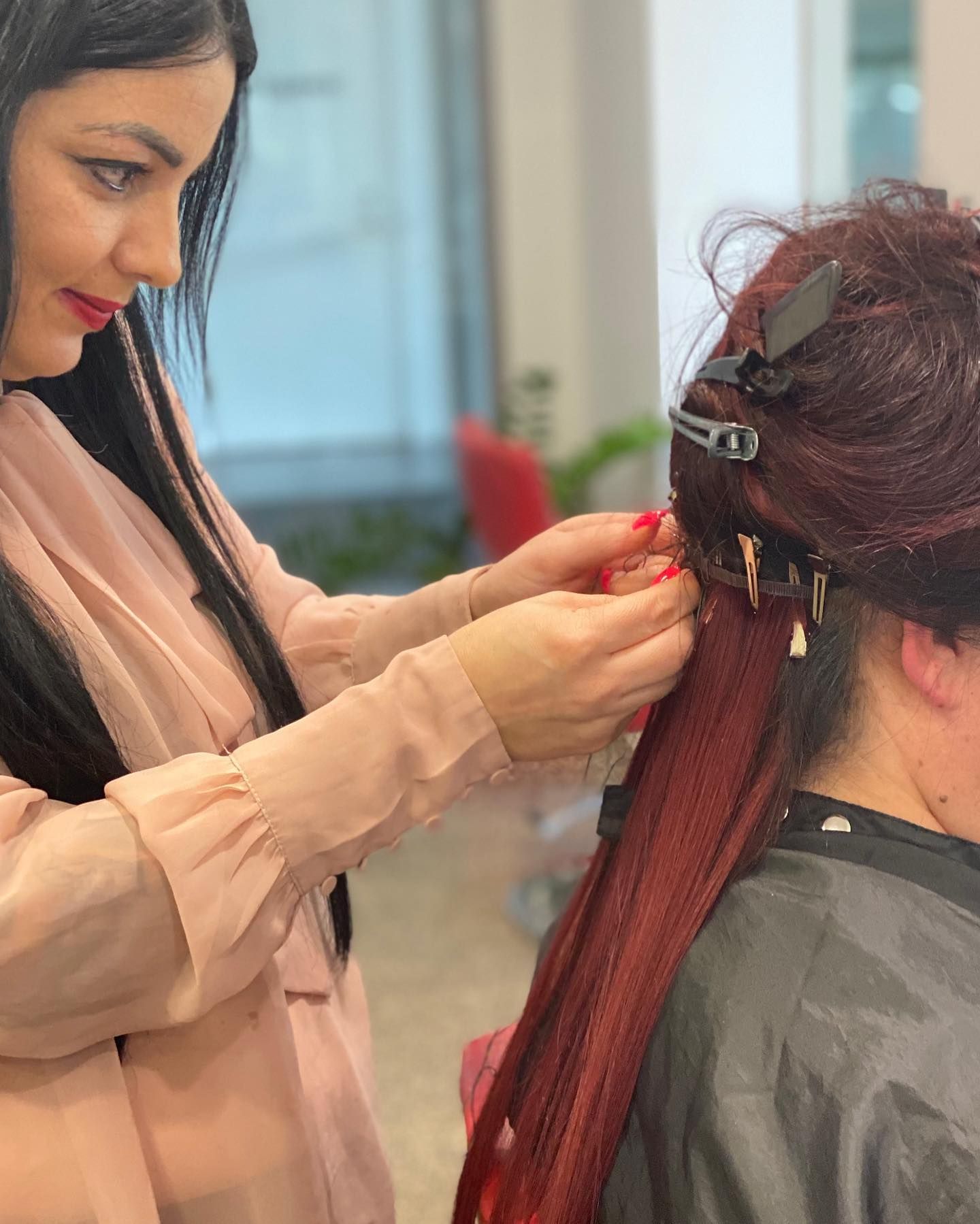 Stylist Secures Red Hair Extensions on a Seated Client in a Salon — Miilan Hair in Darwin City, NT