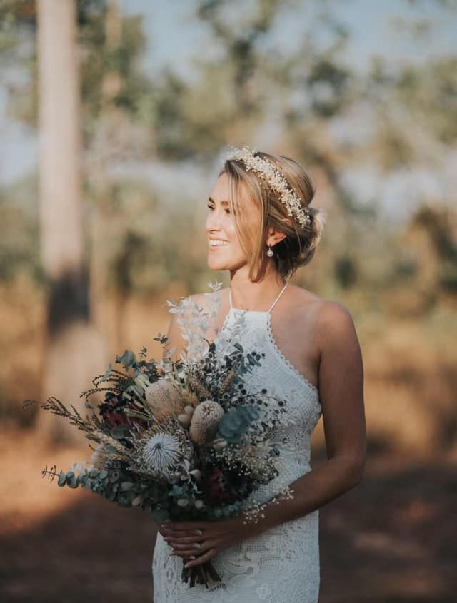 Bride in a White Lace Dress Holding a Bouquet Outdoors, With Soft Sunlight and Blurred Trees — Miilan Hair in Darwin City, NT