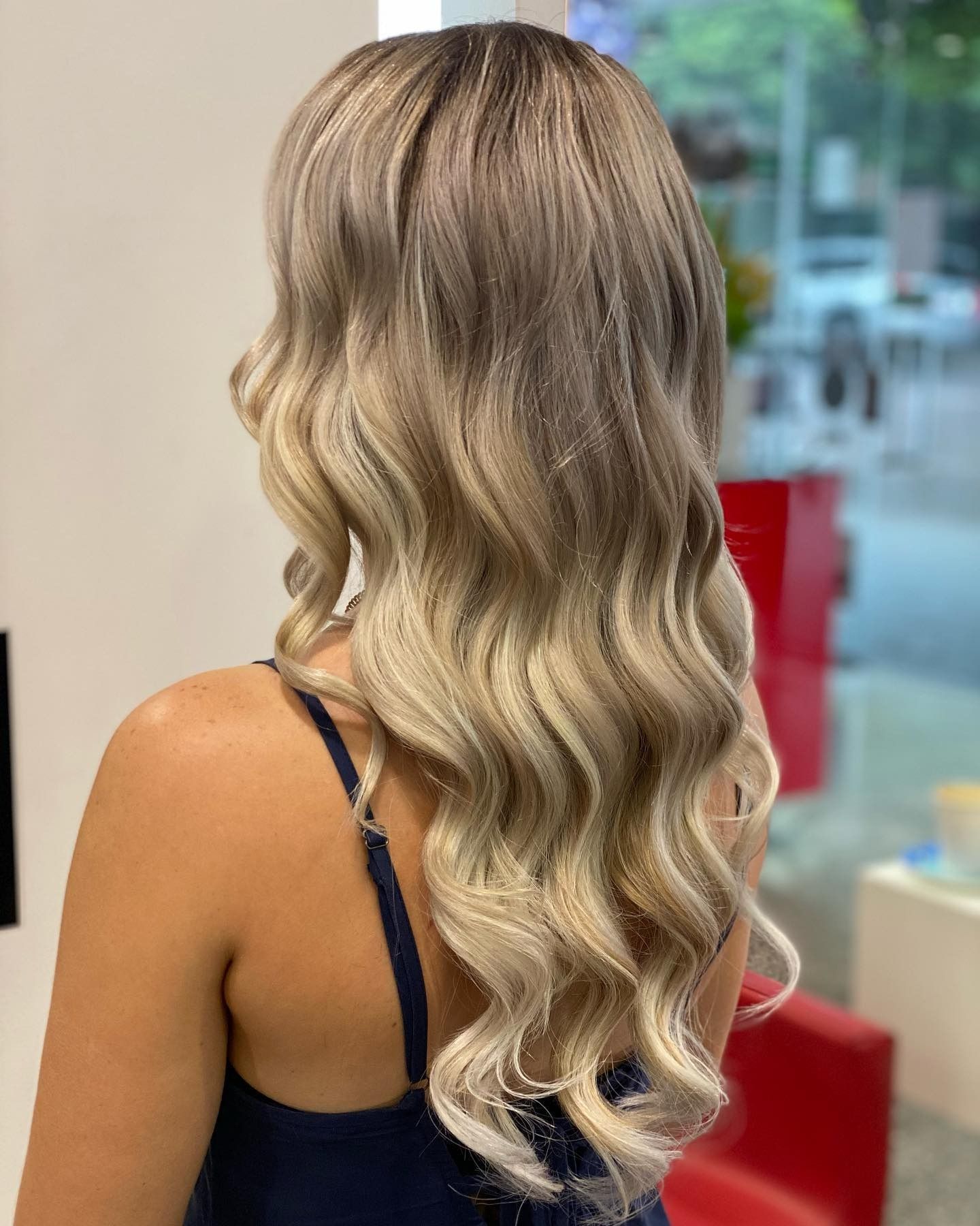 Side Profile of a Woman With Blonde Wavy Hair in a Salon, With Red Counters — Miilan Hair in Darwin City, NT