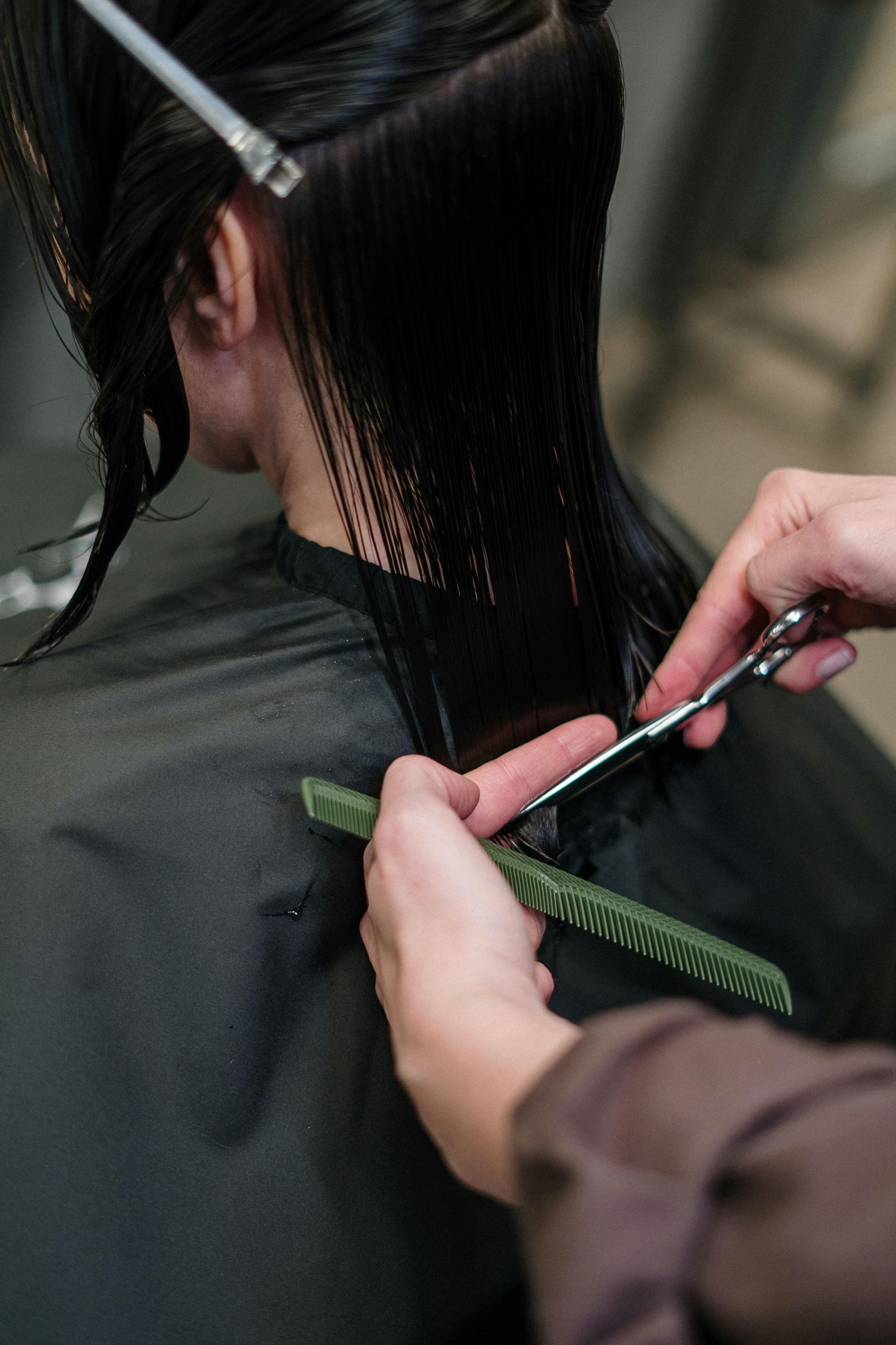 Hairdresser Trimming Dark Hair With Scissors and Comb Under a Black Salon Cape — Miilan Hair in Darwin City, NT