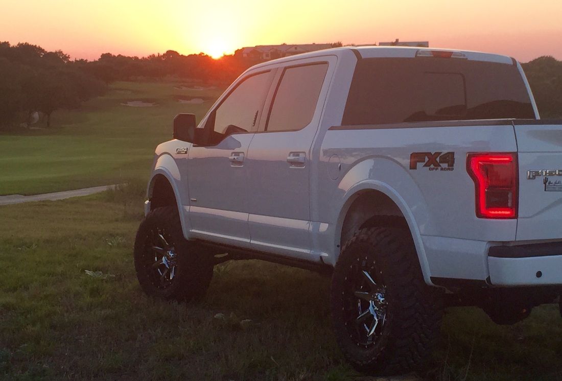 A white truck is parked in a grassy field at sunset.