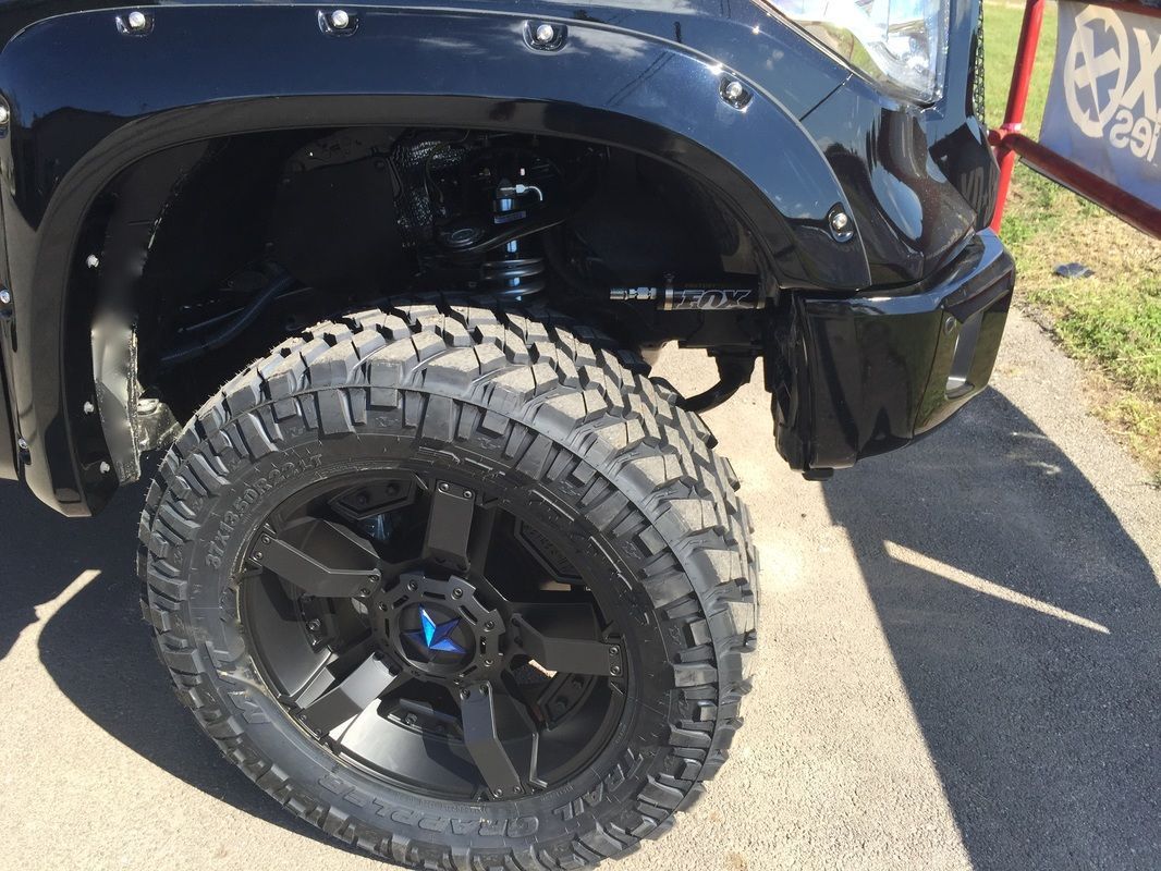 A black truck with black wheels and tires is parked on the side of the road.
