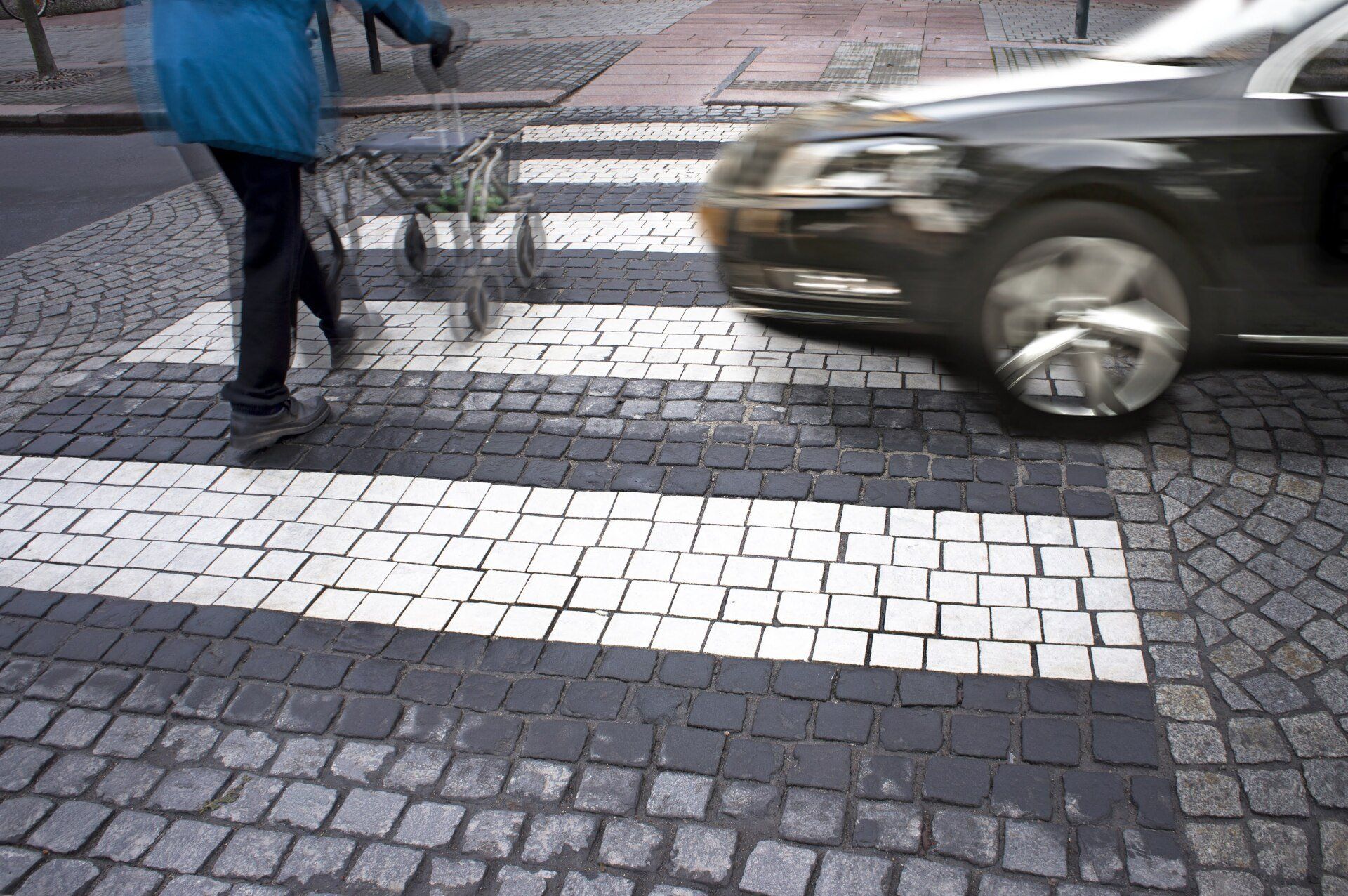 A black car is driving past a person crossing the street