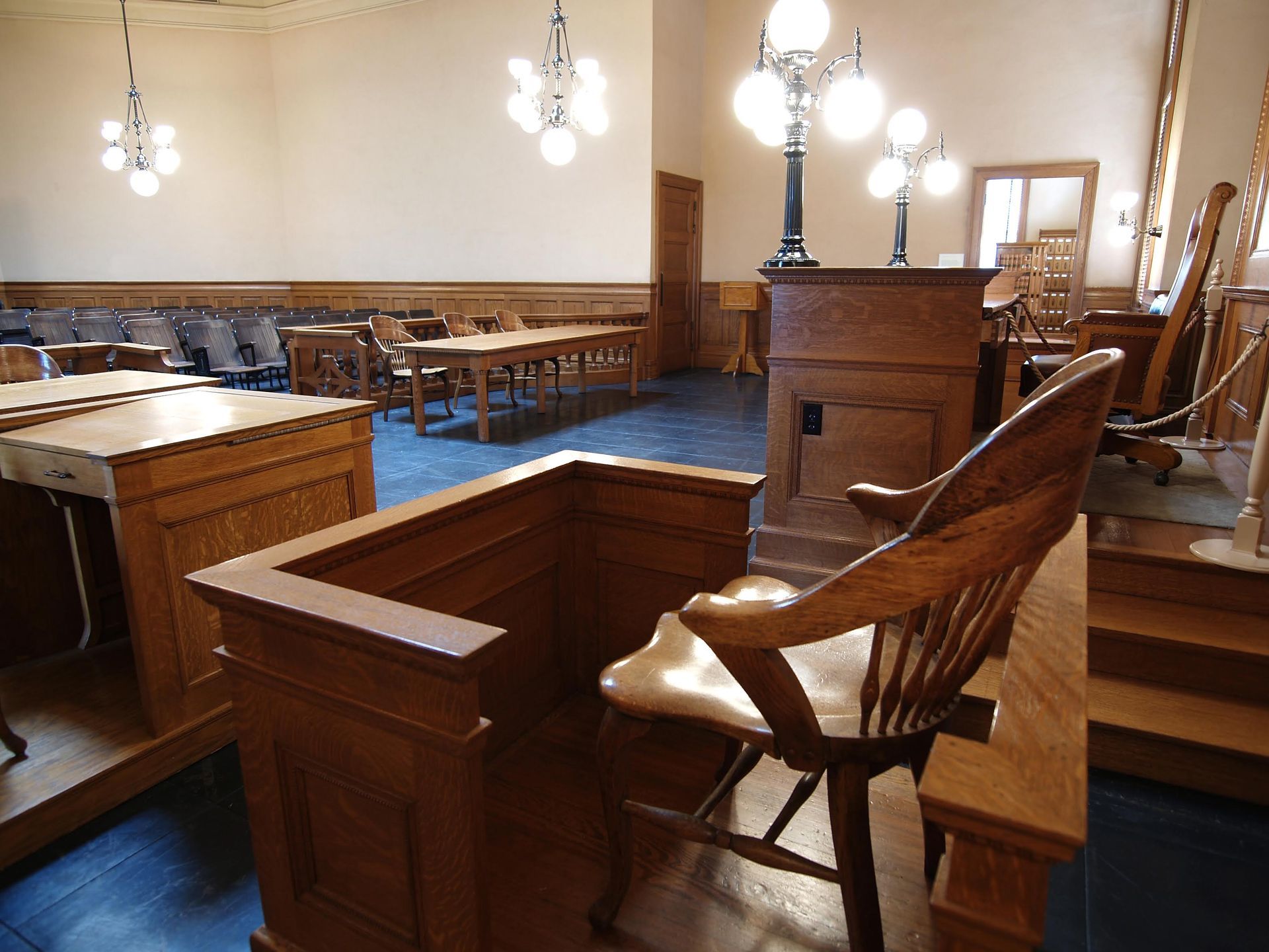 A wooden chair in a courtroom with tables and chairs