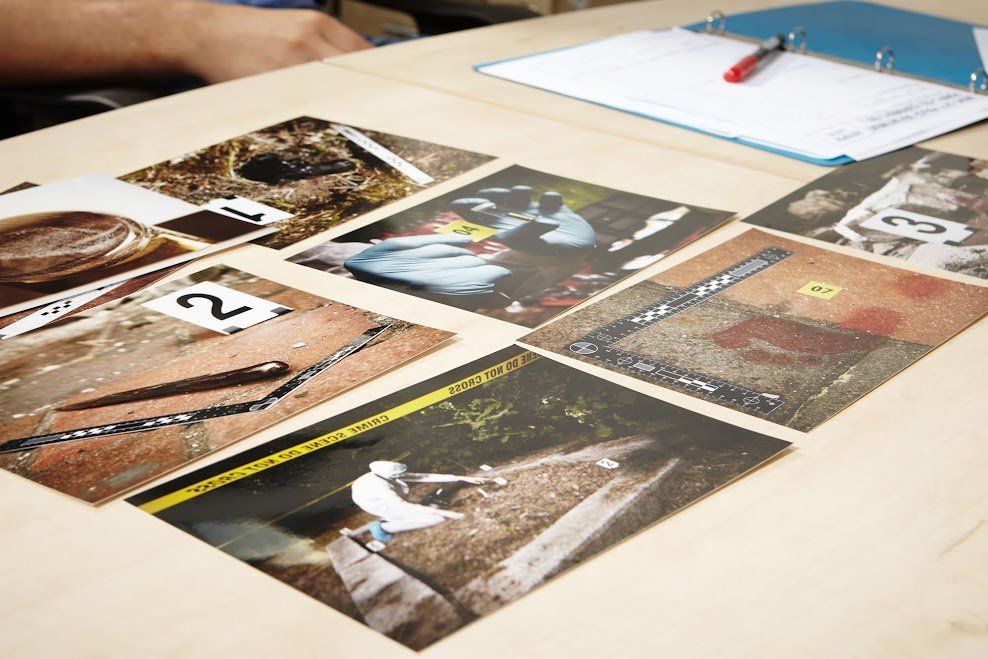 Photos of crime scene evidence laid out on a table, including what appears to be a body, tools, and a gun.
