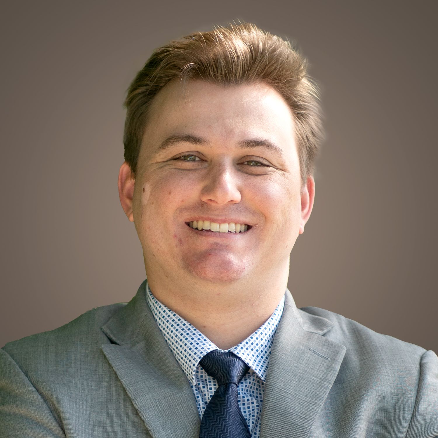 Man in a gray suit and patterned shirt smiles, headshot.