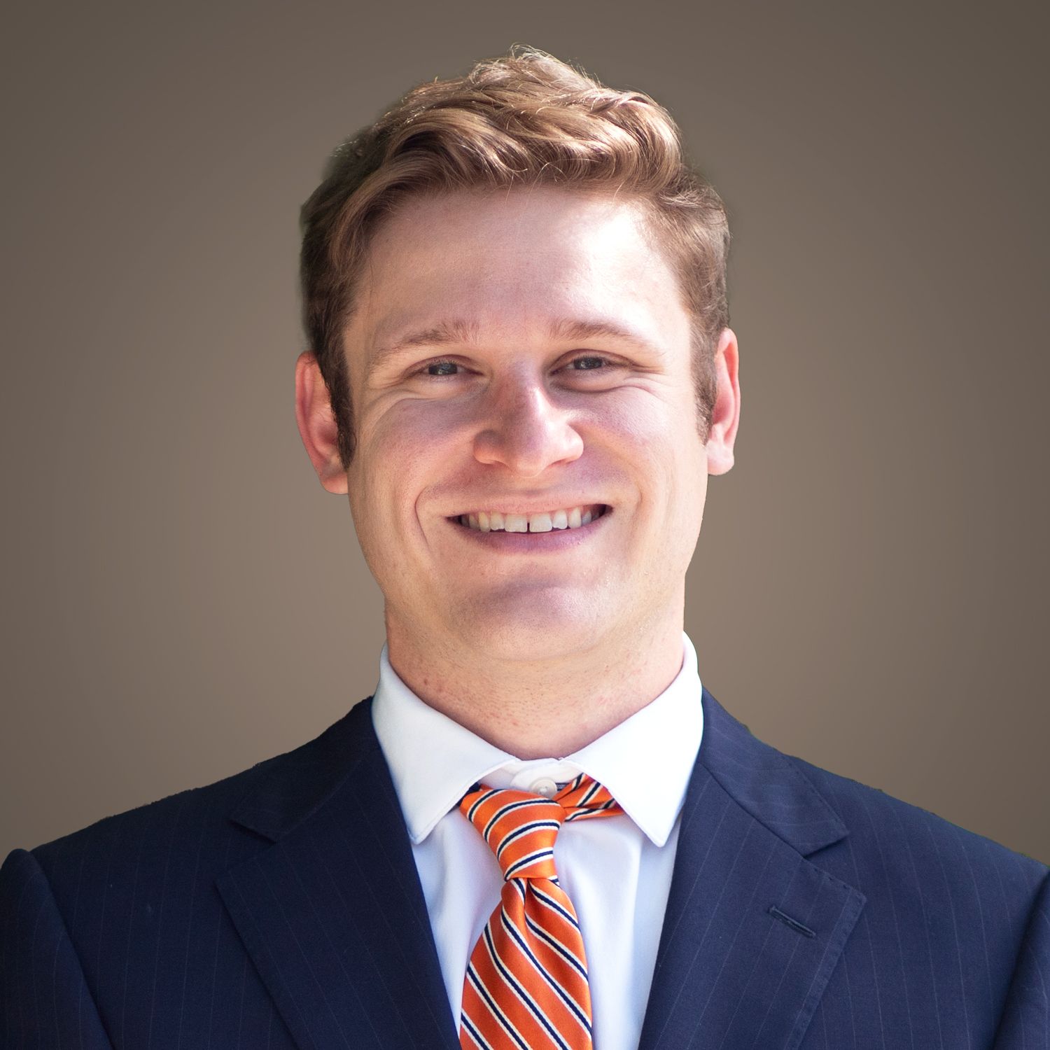 Man in a suit smiles at the camera, wearing an orange and white striped tie.