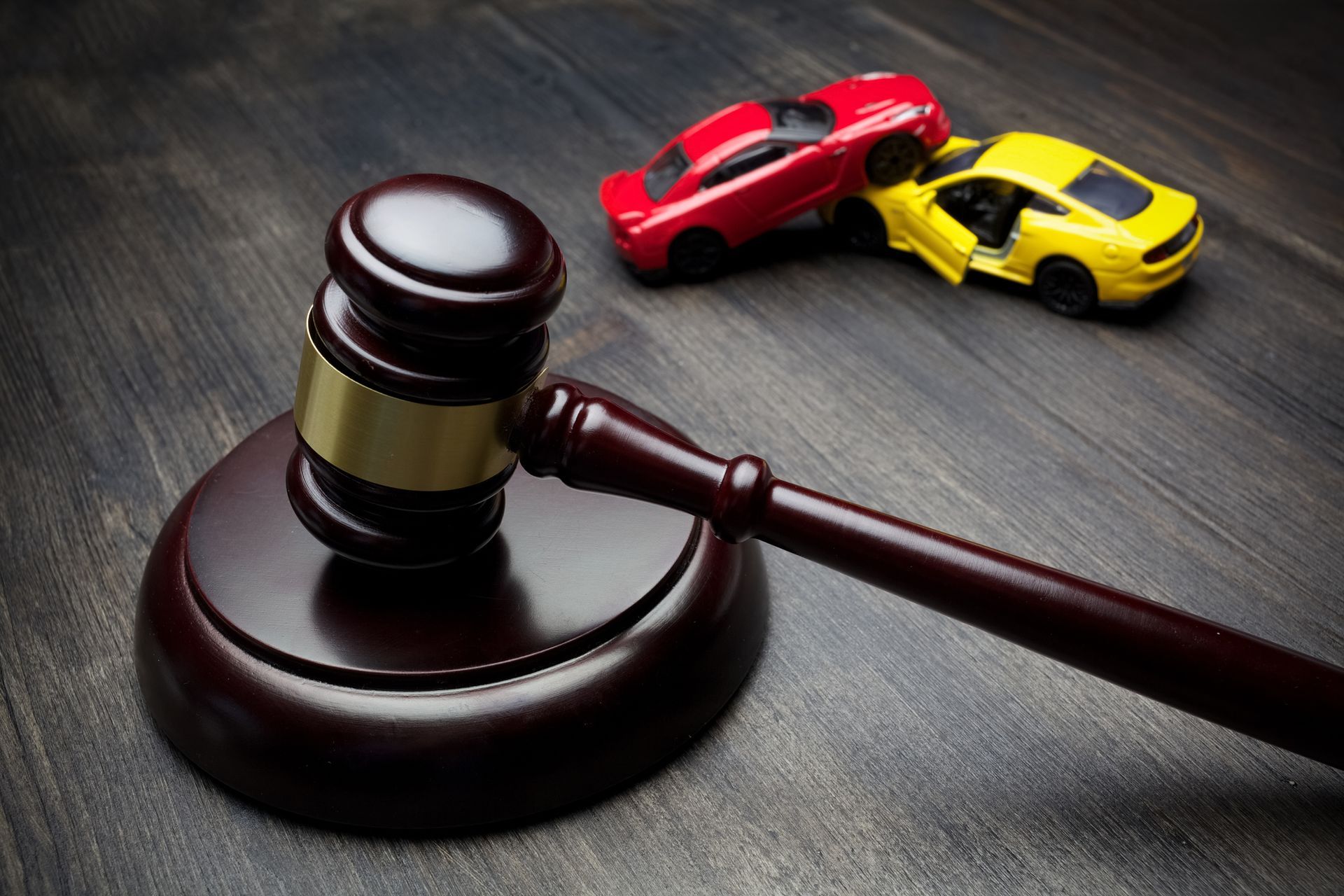 Two toy cars & a judge’s gavel on a wooden table illustrate the concept of a car accident lawyer.