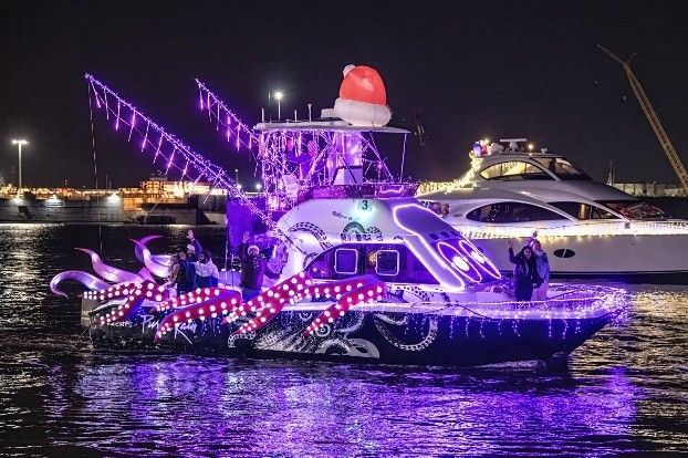 Festive boat parade with a boat decorated as an octopus in purple lights, wearing a Santa hat. Festive boat parade with a boat decorated as an octopus in purple lights, wearing a Santa hat.