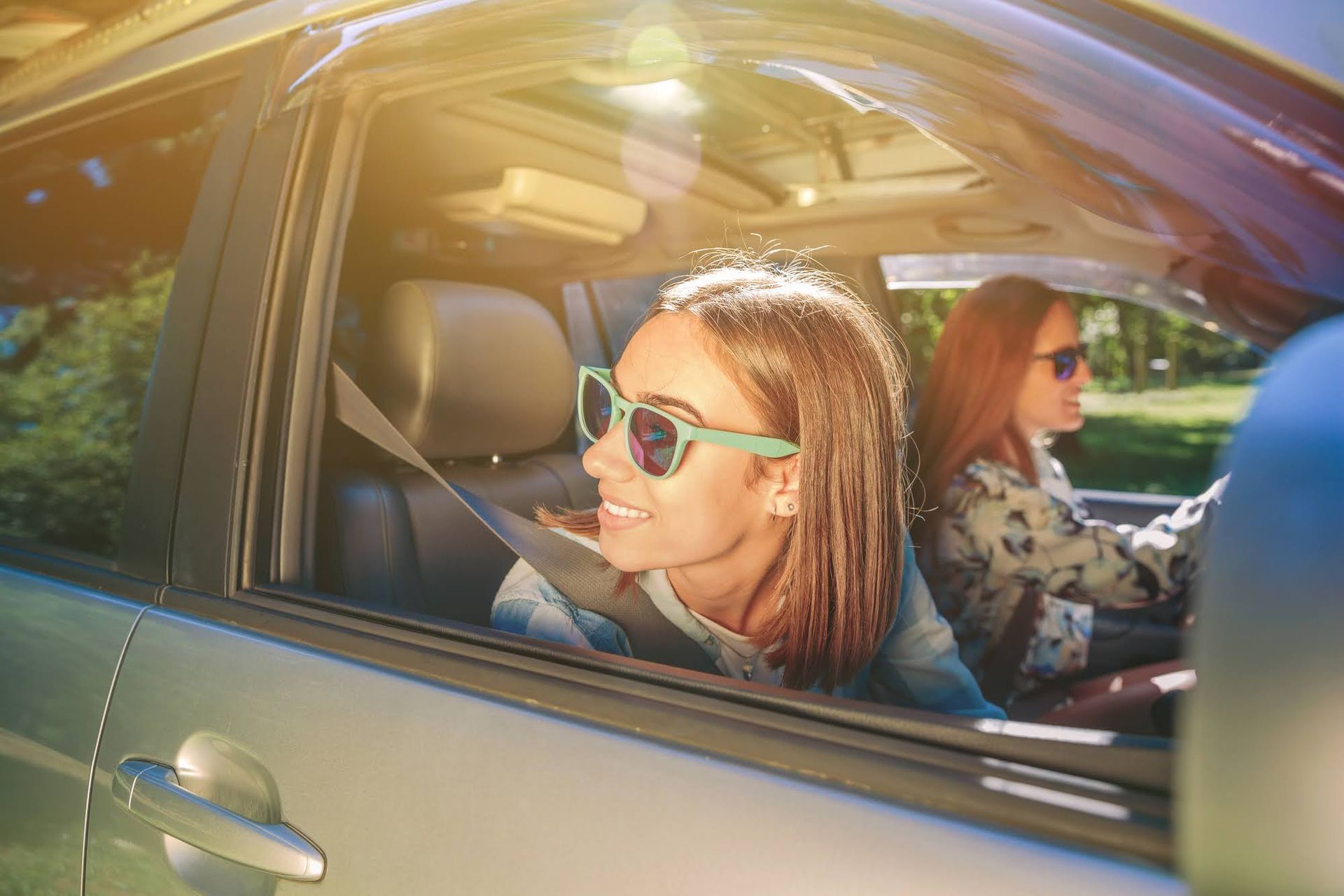 Two women are sitting in a car wearing sunglasses.