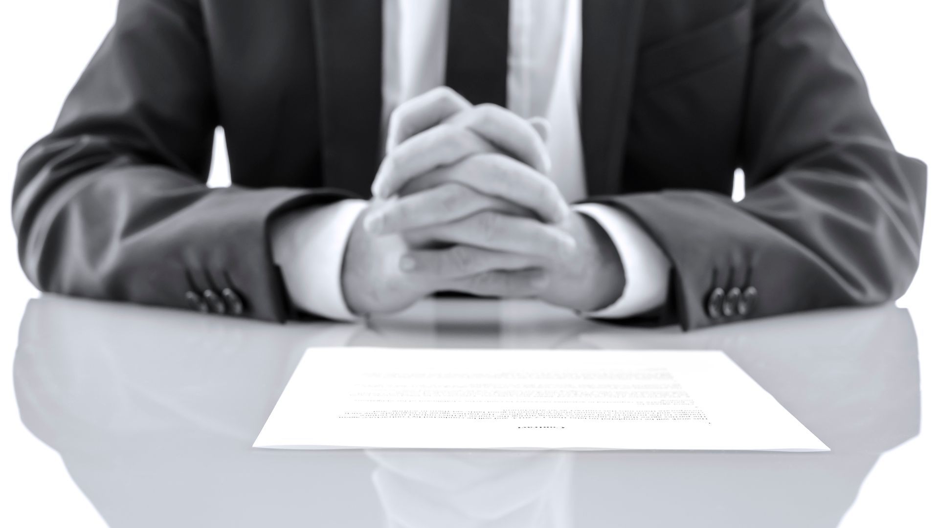 Man in suit, hands clasped on table over document.