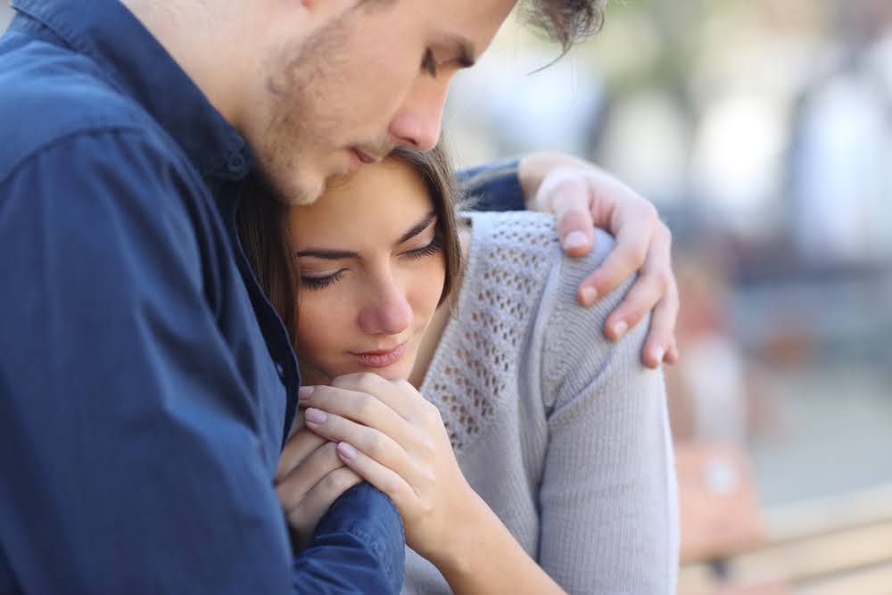 A man is comforting a woman who is sitting on a bench.
