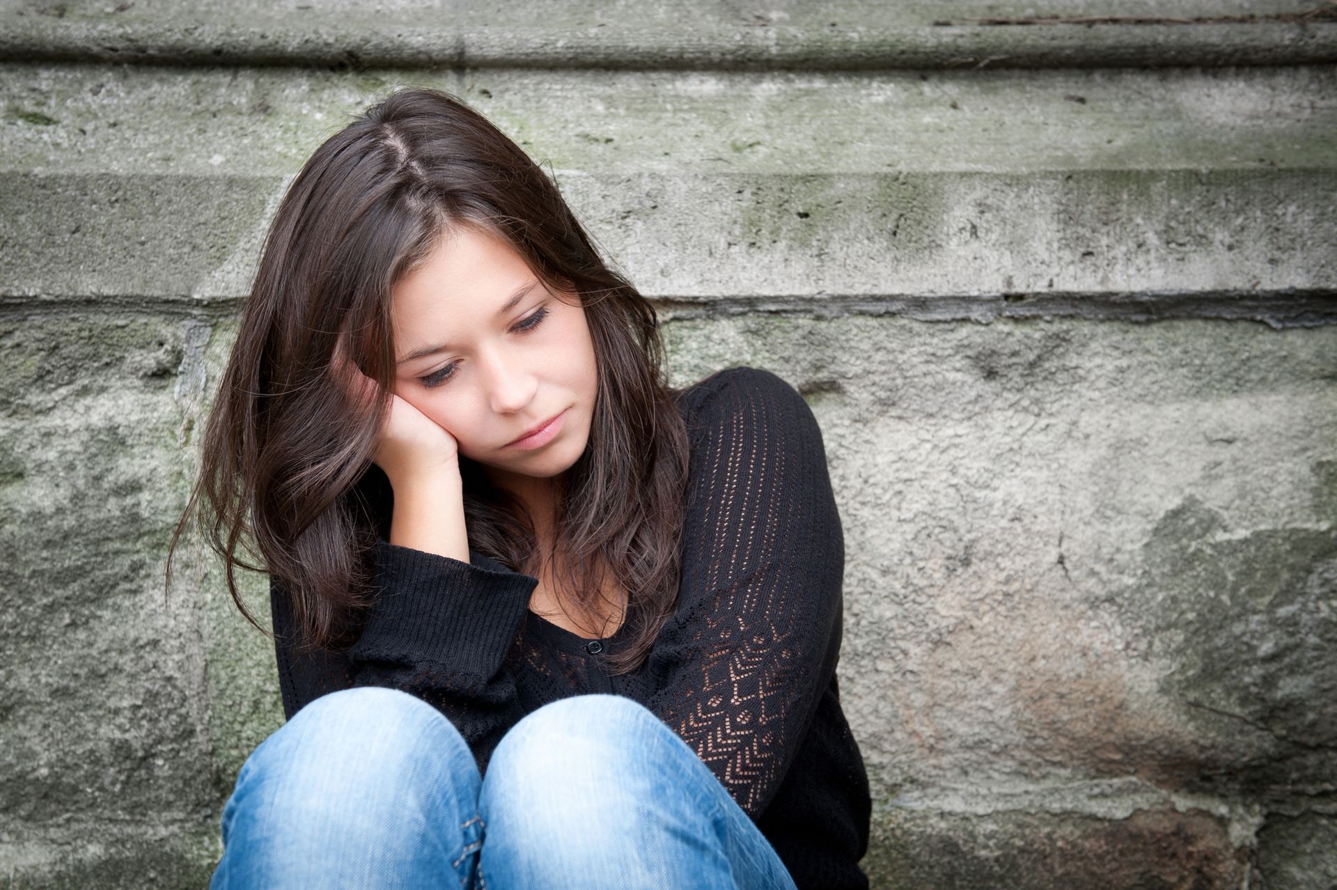 A young woman is sitting on a set of stairs with her head resting on her hand.