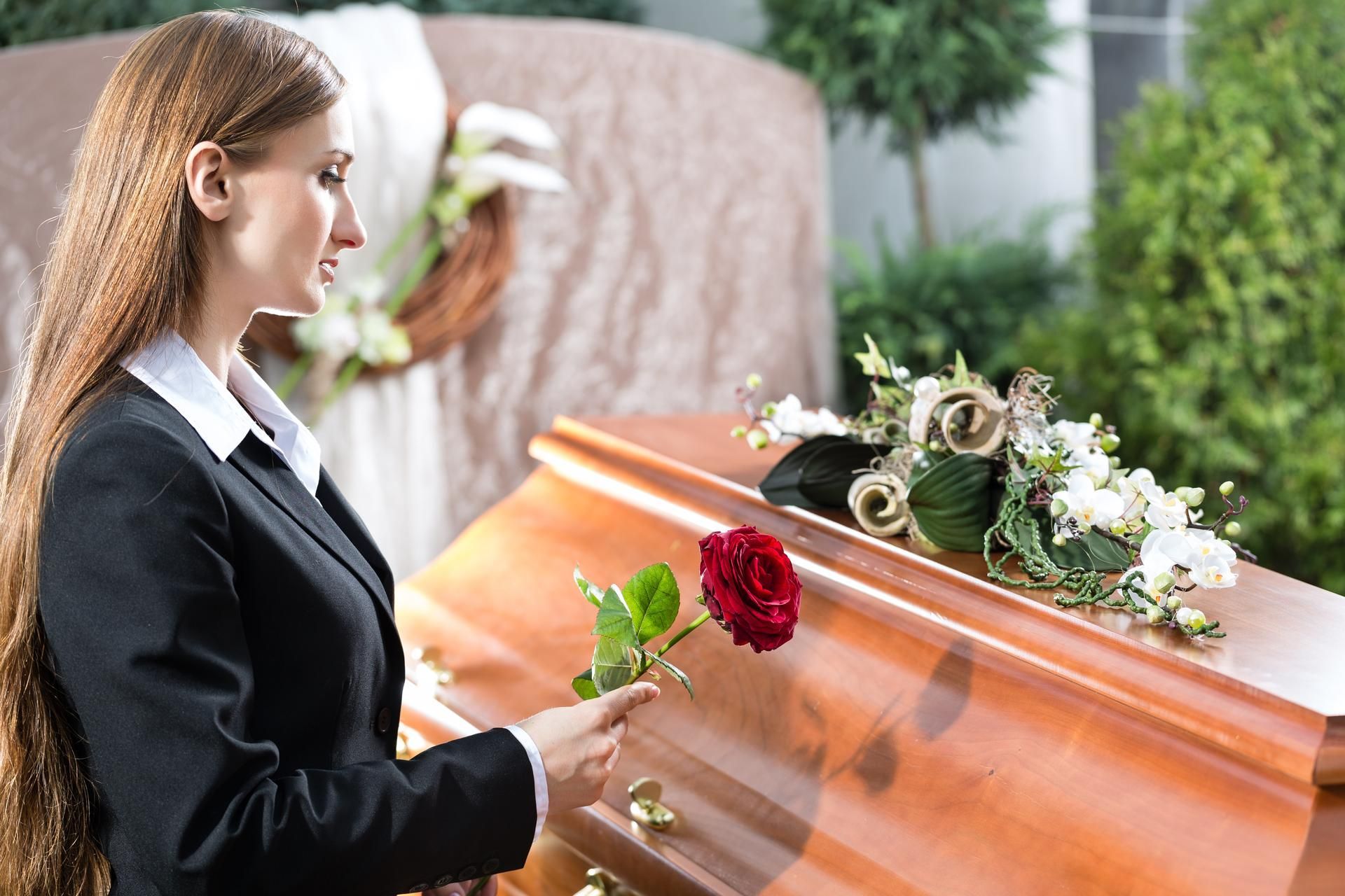 A woman is holding a rose in front of a coffin at a funeral.