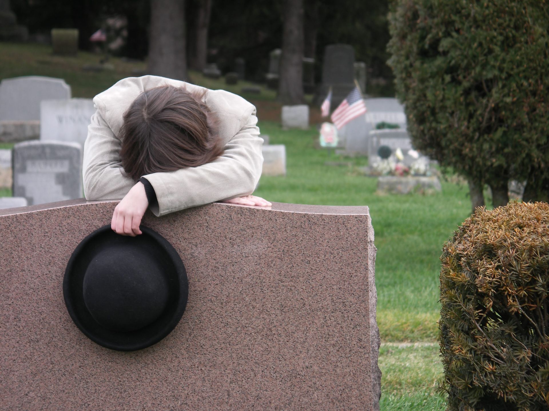 A person laying on a grave with a hat on it