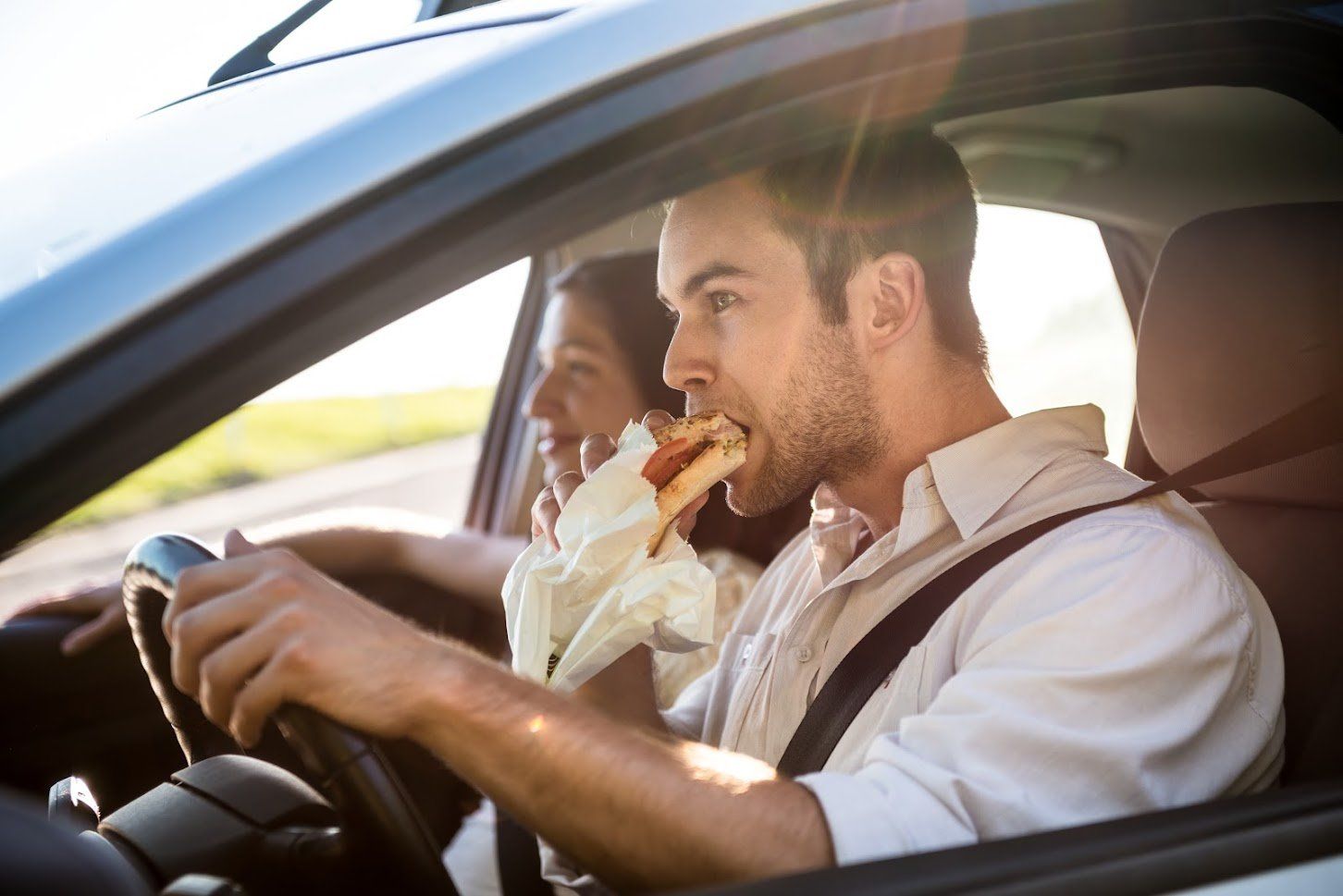 A man is eating a hot dog while driving a car.