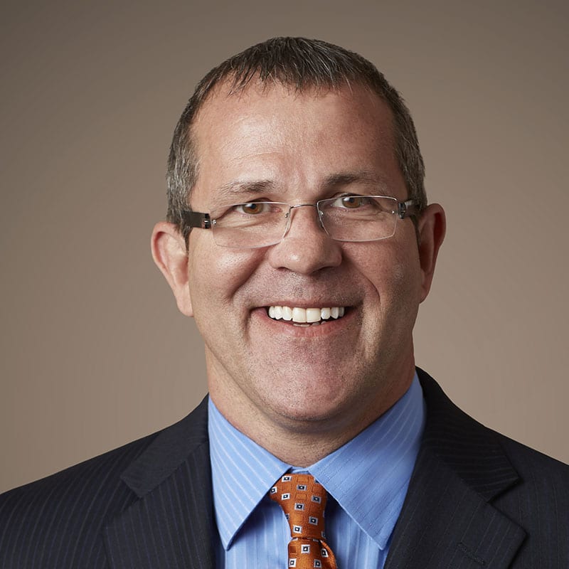 Man wearing glasses and a suit smiles at the camera.