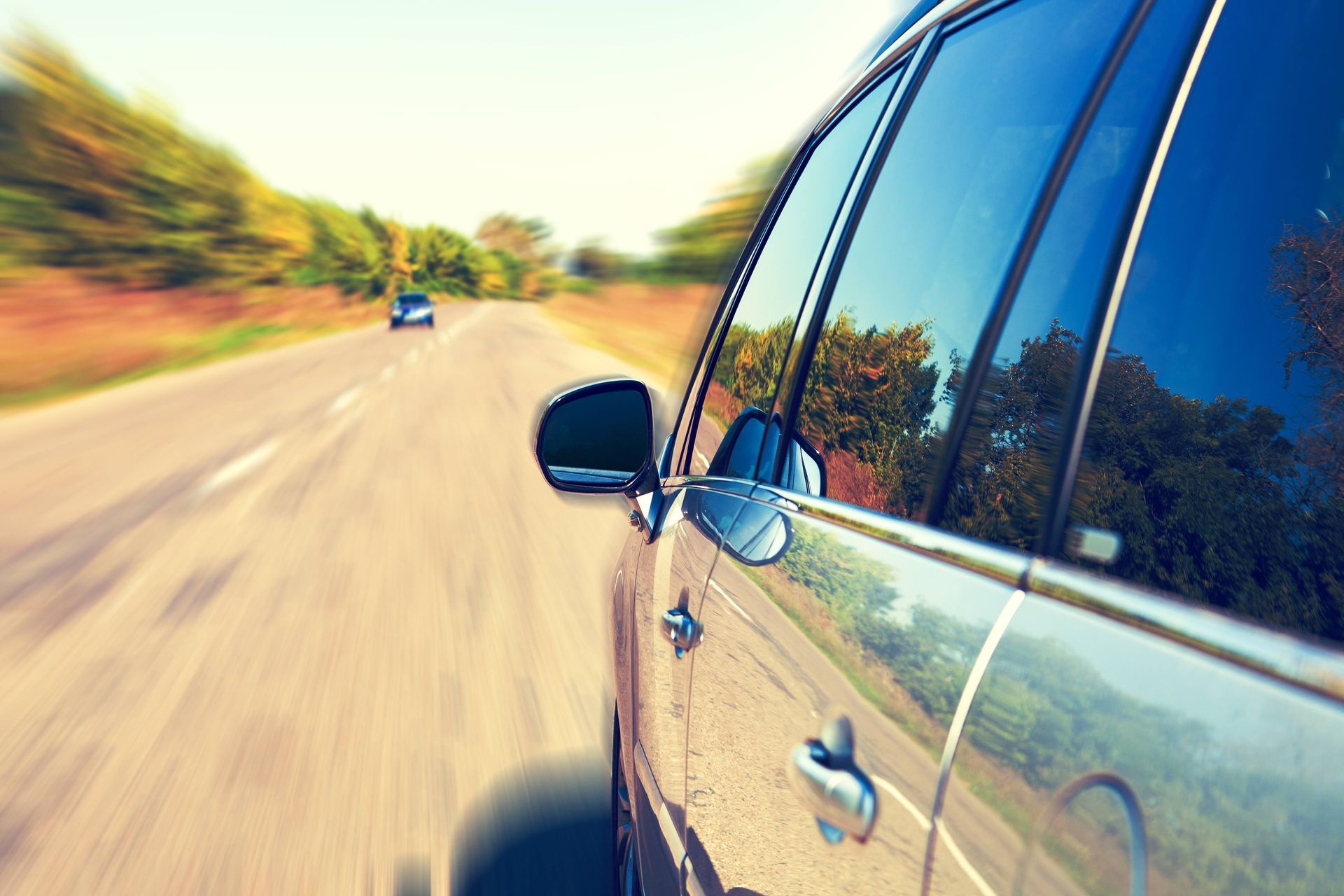 A car is driving down a road with trees in the background.