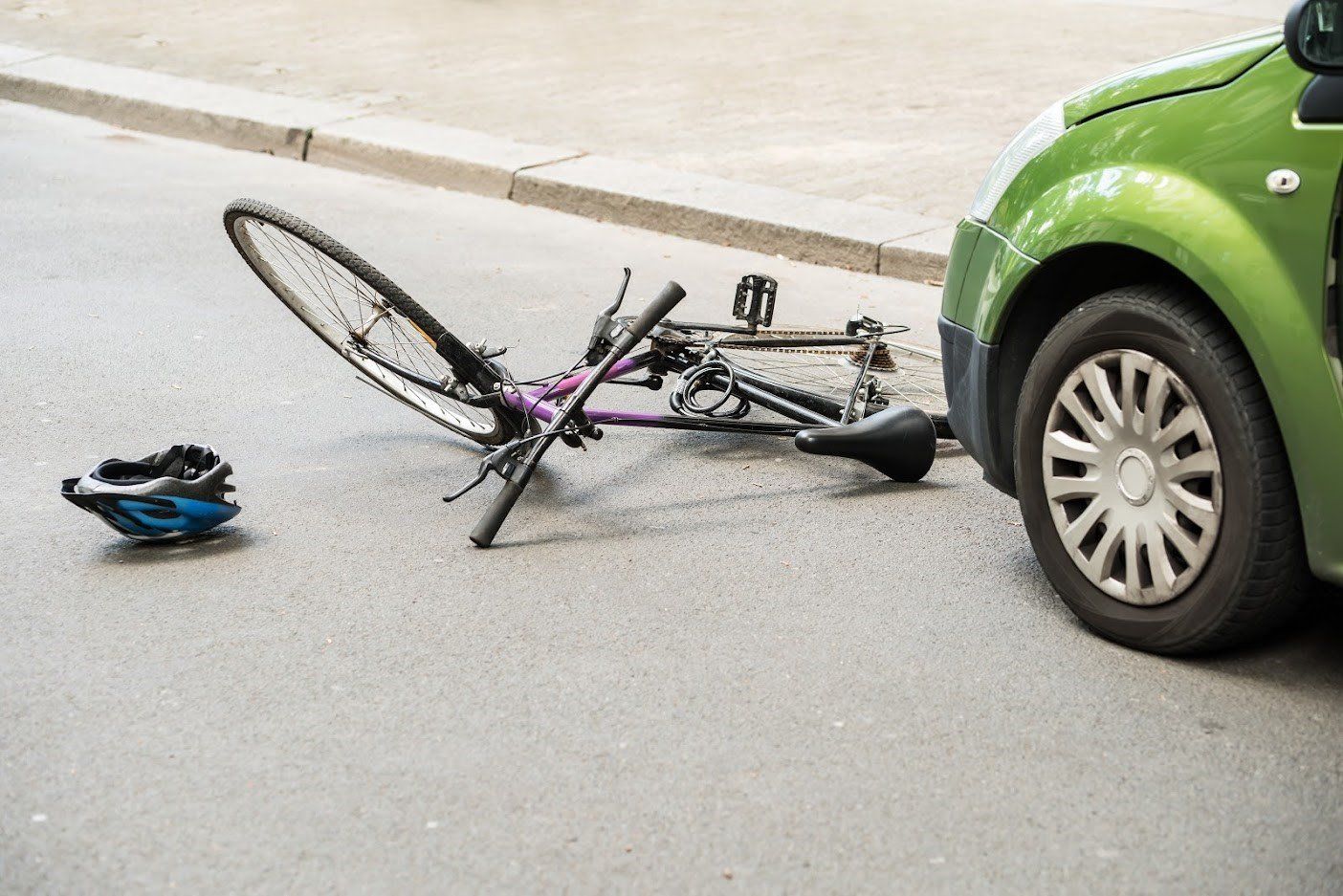 A bicycle is laying on the ground next to a green car.
