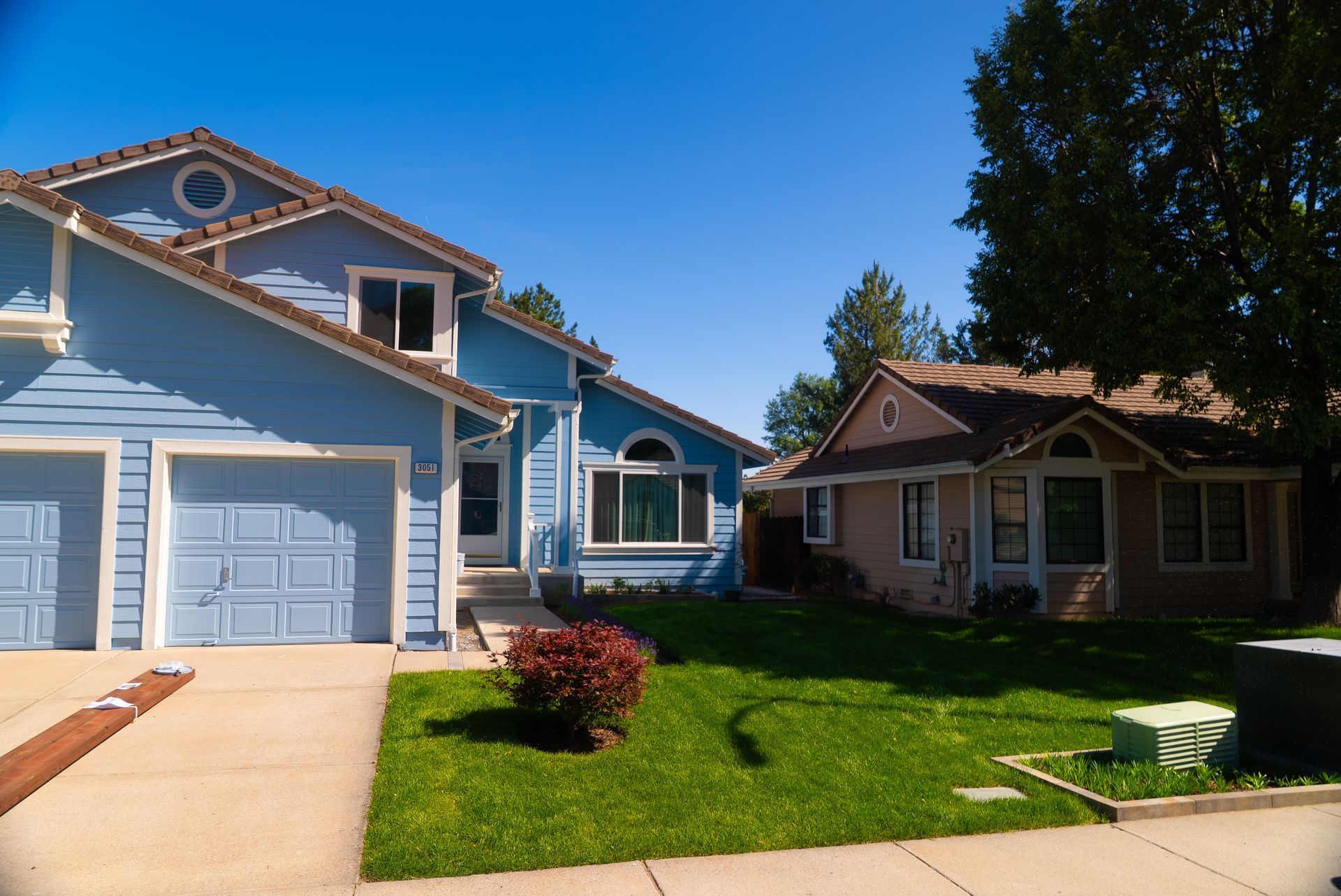 Blue and tan houses with green lawns under a bright blue sky.