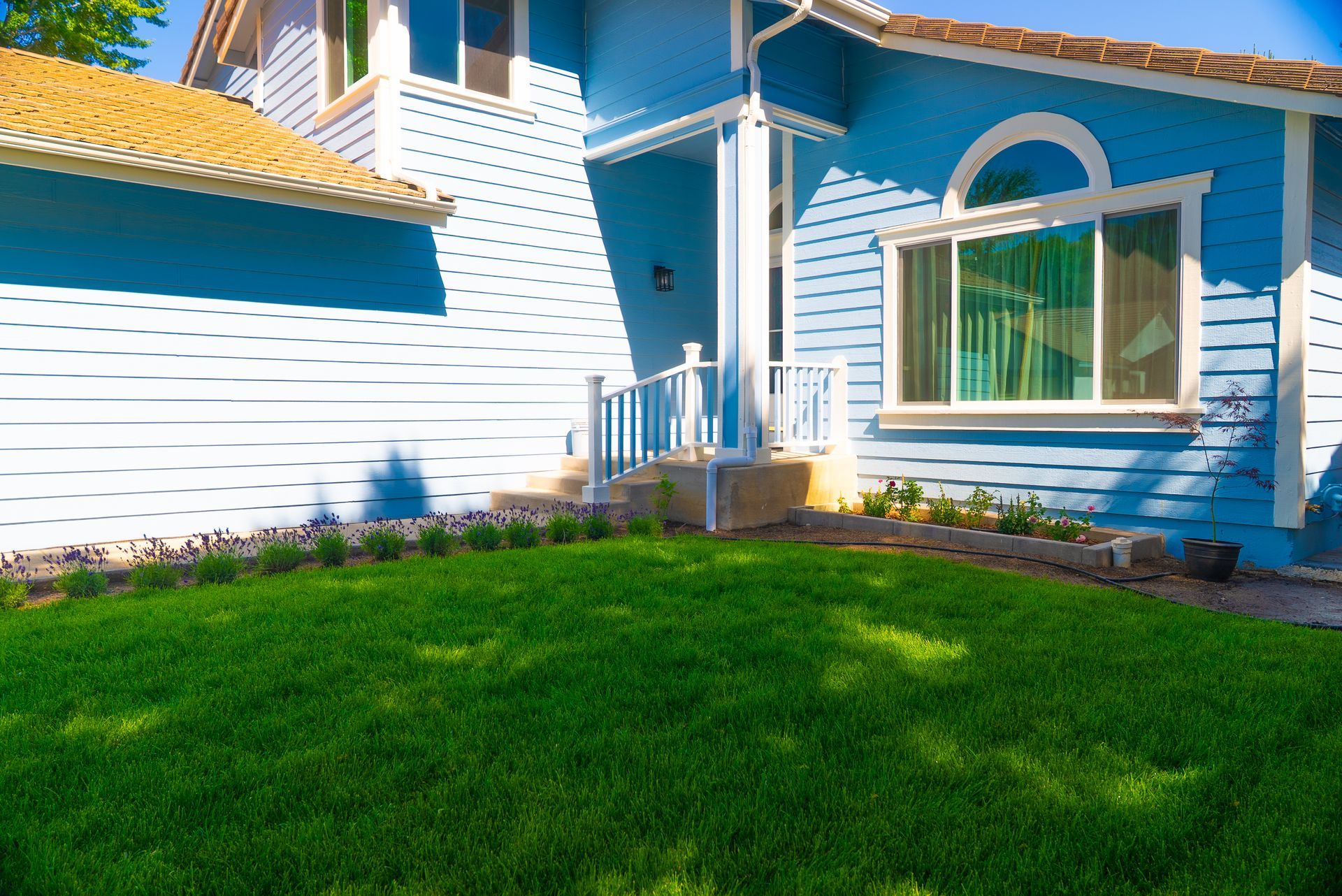 A bright blue house with horizontal siding and a green lawn, featuring an arched window and a front porch entryway.