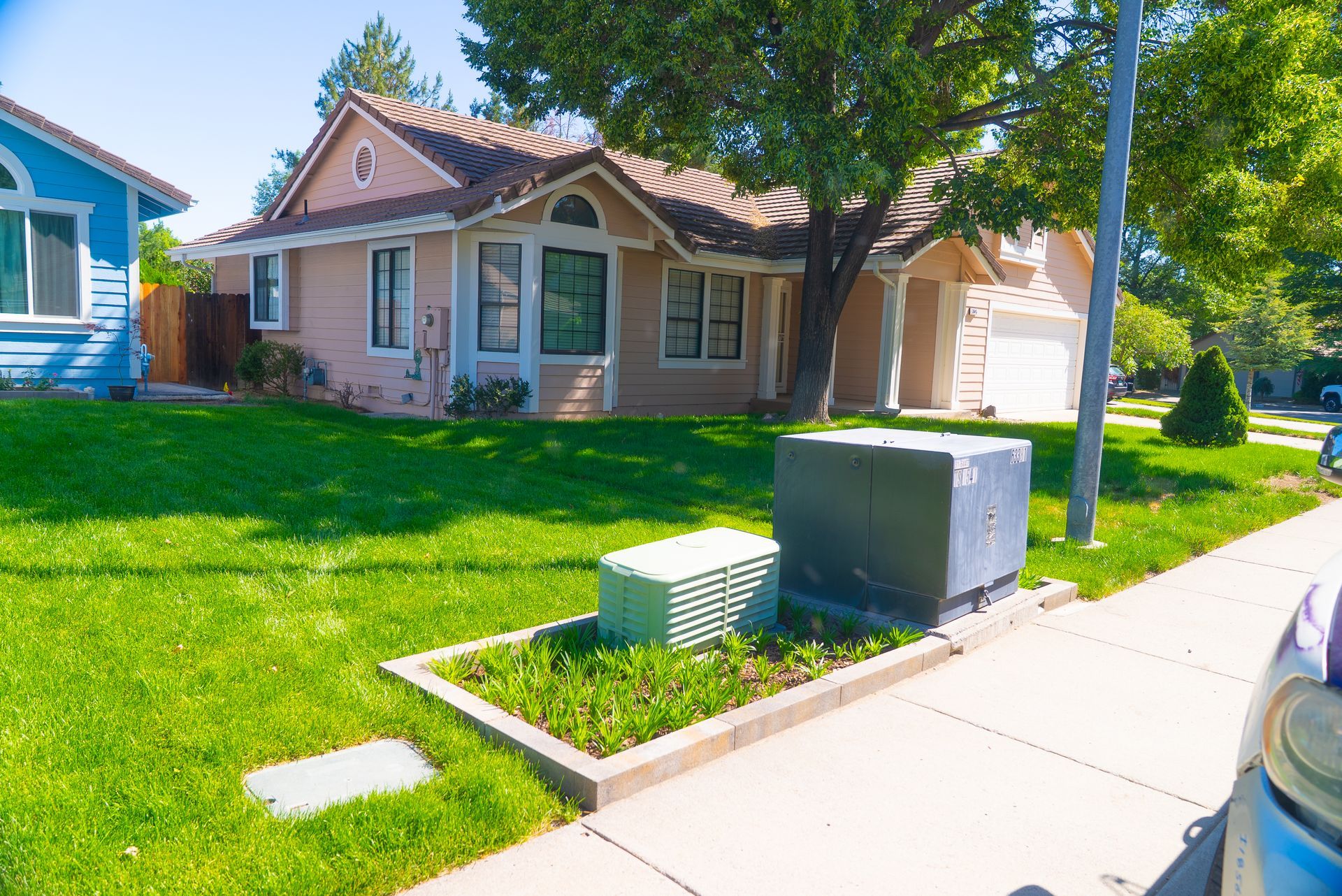 A house with pink siding and a green lawn, sidewalk in front, and utility boxes.