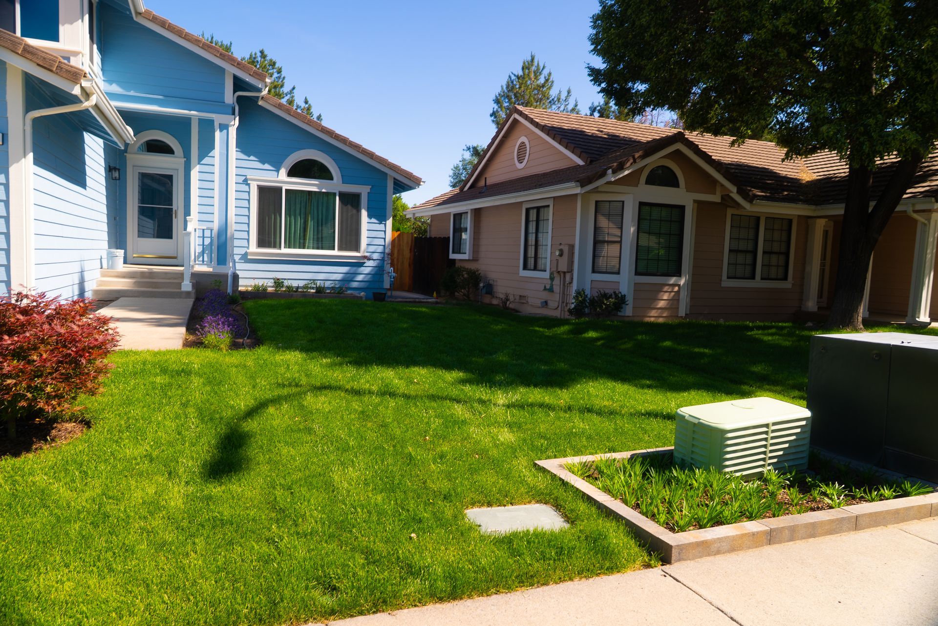 Houses with blue and tan exteriors, lush green lawn, and a clear blue sky.