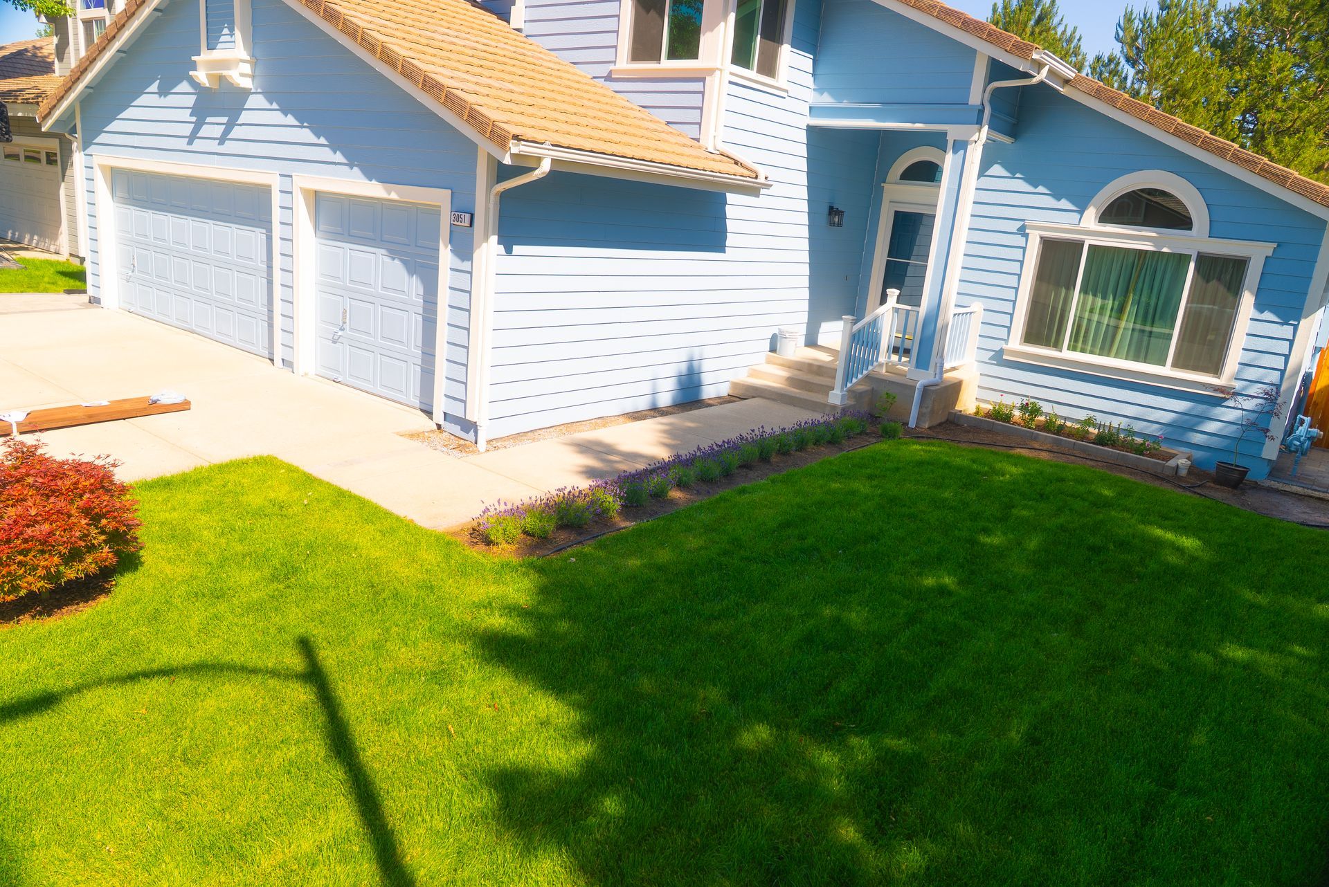 Blue house with two-car garage, lush green lawn, and a small flower bed. Sunny day.