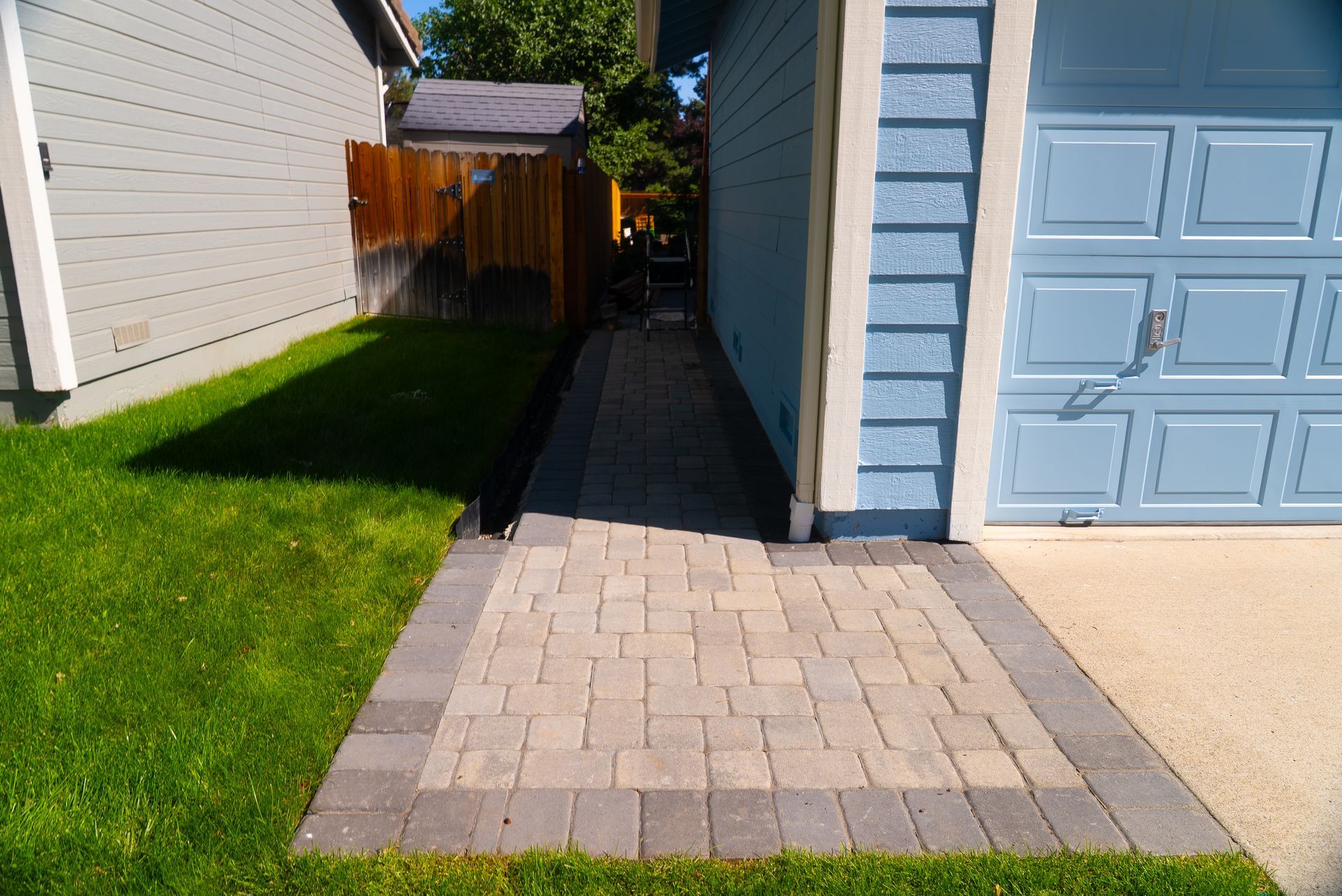 Brick pathway beside a blue garage and a grassy yard.