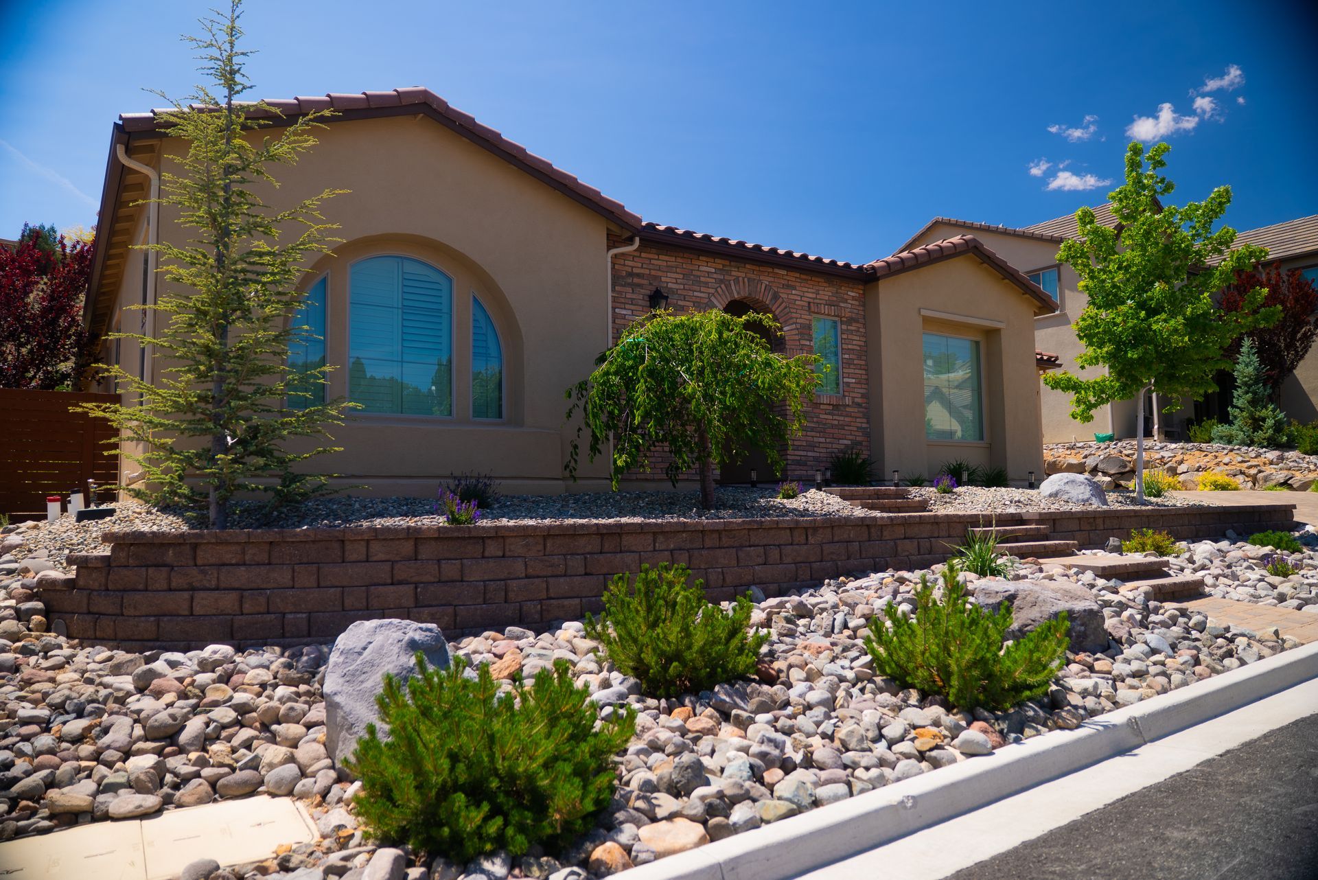 Tan stucco home with stone accents and drought-tolerant landscaping under a blue sky.