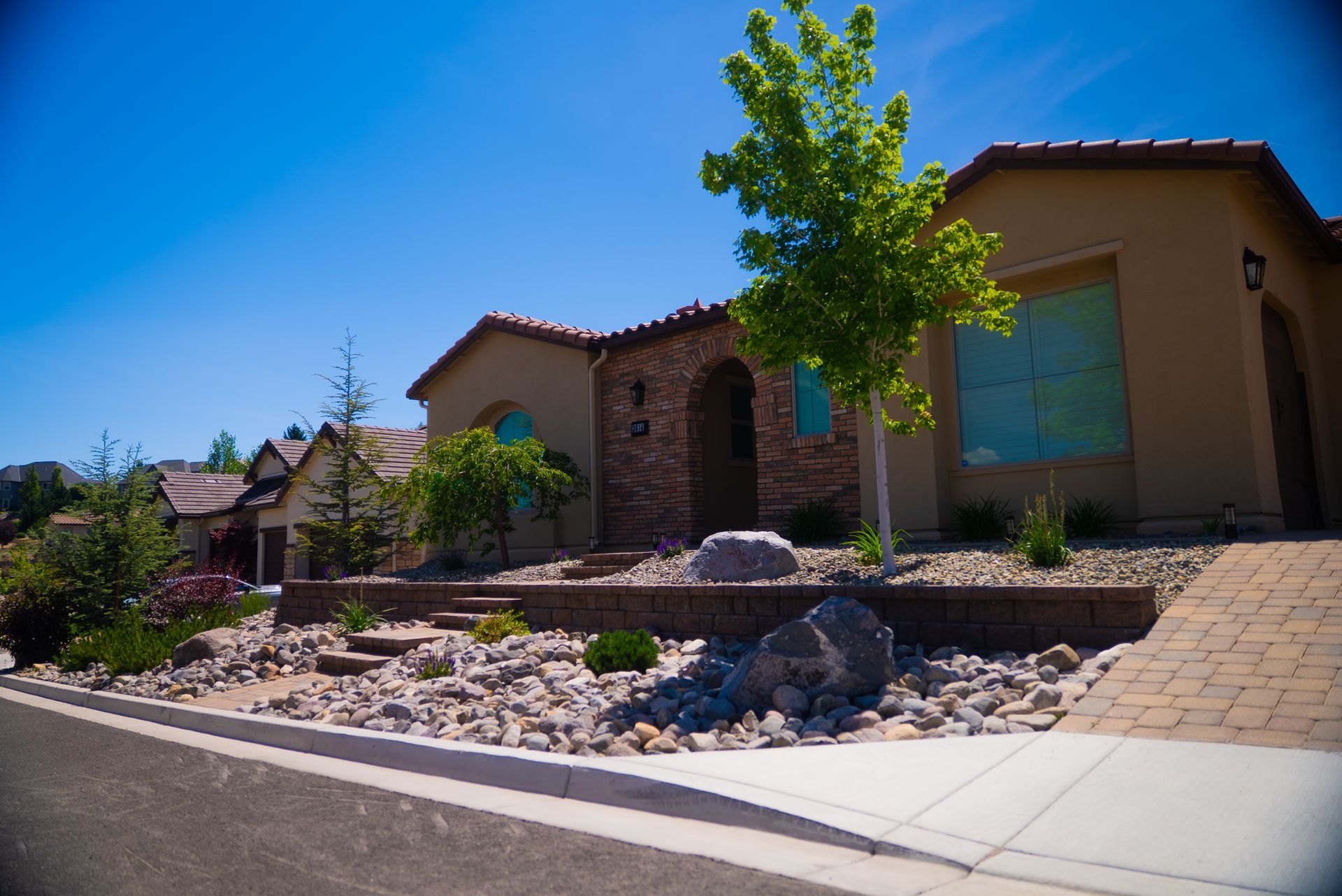 Beige house with a stone facade, low-water landscaping, and a blue sky - service by Activescapes.