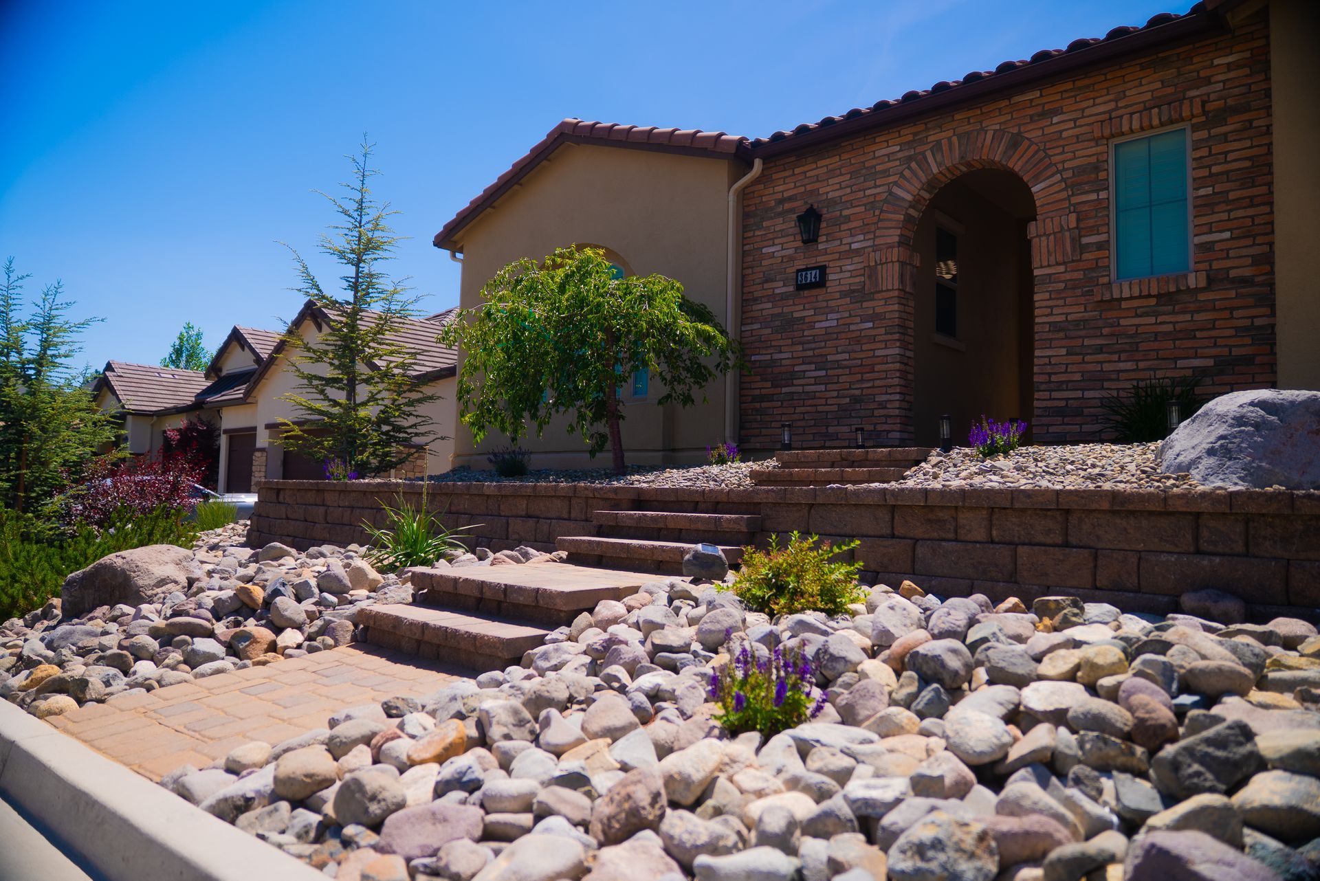 Brick house with stone steps and landscaping; blue sky.