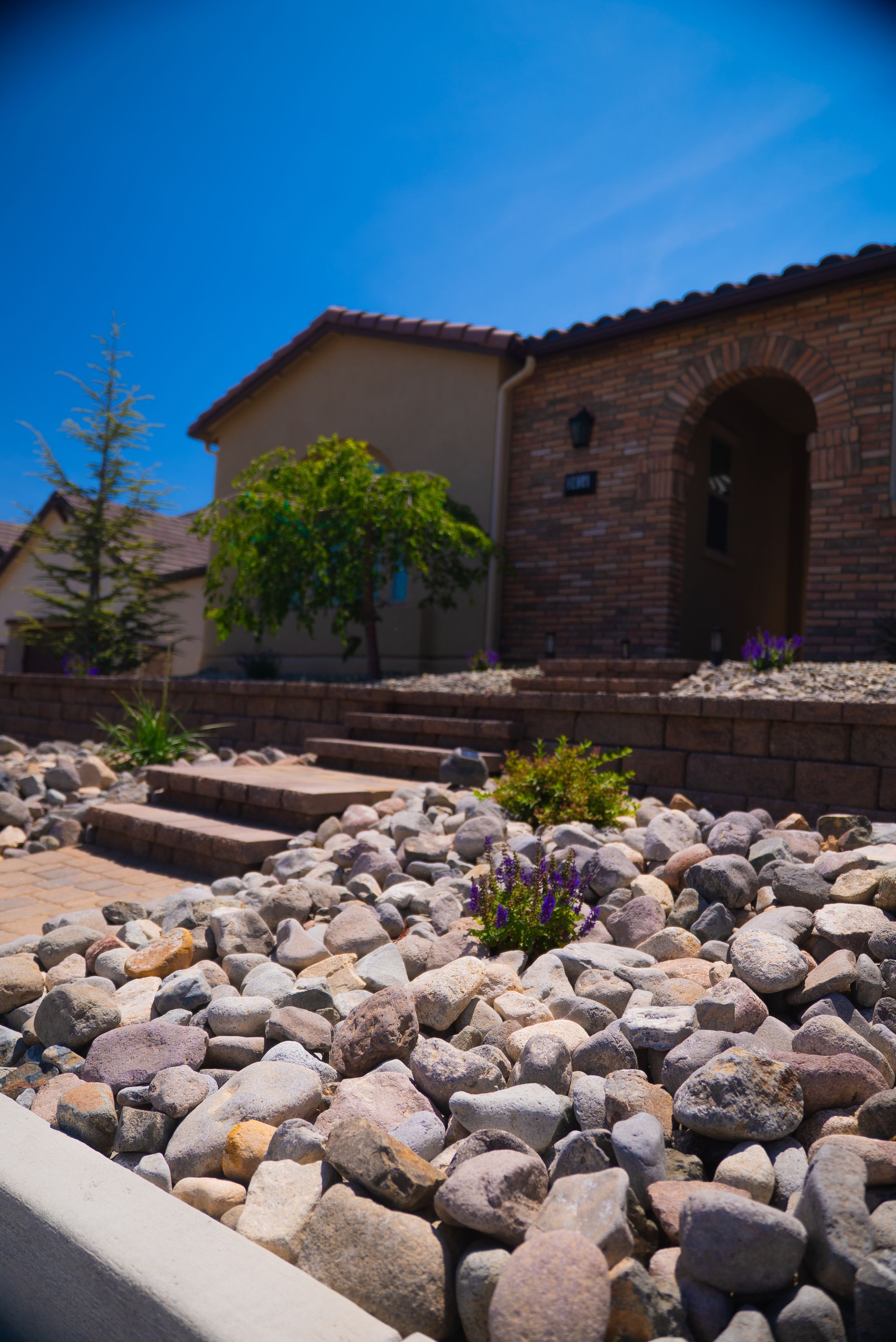 House with stone steps and rock landscaping under a bright blue sky - service by Activescapes.