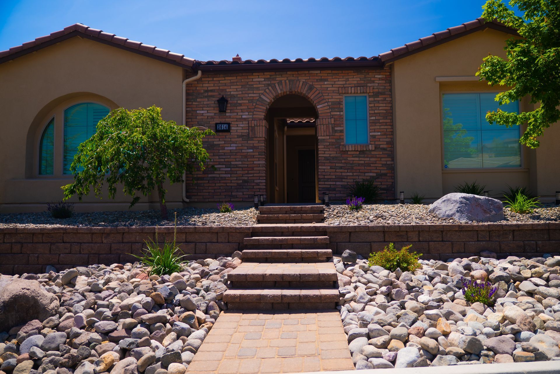 Tan house with stone and brick facade, steps leading to entrance, and rock landscaping.
